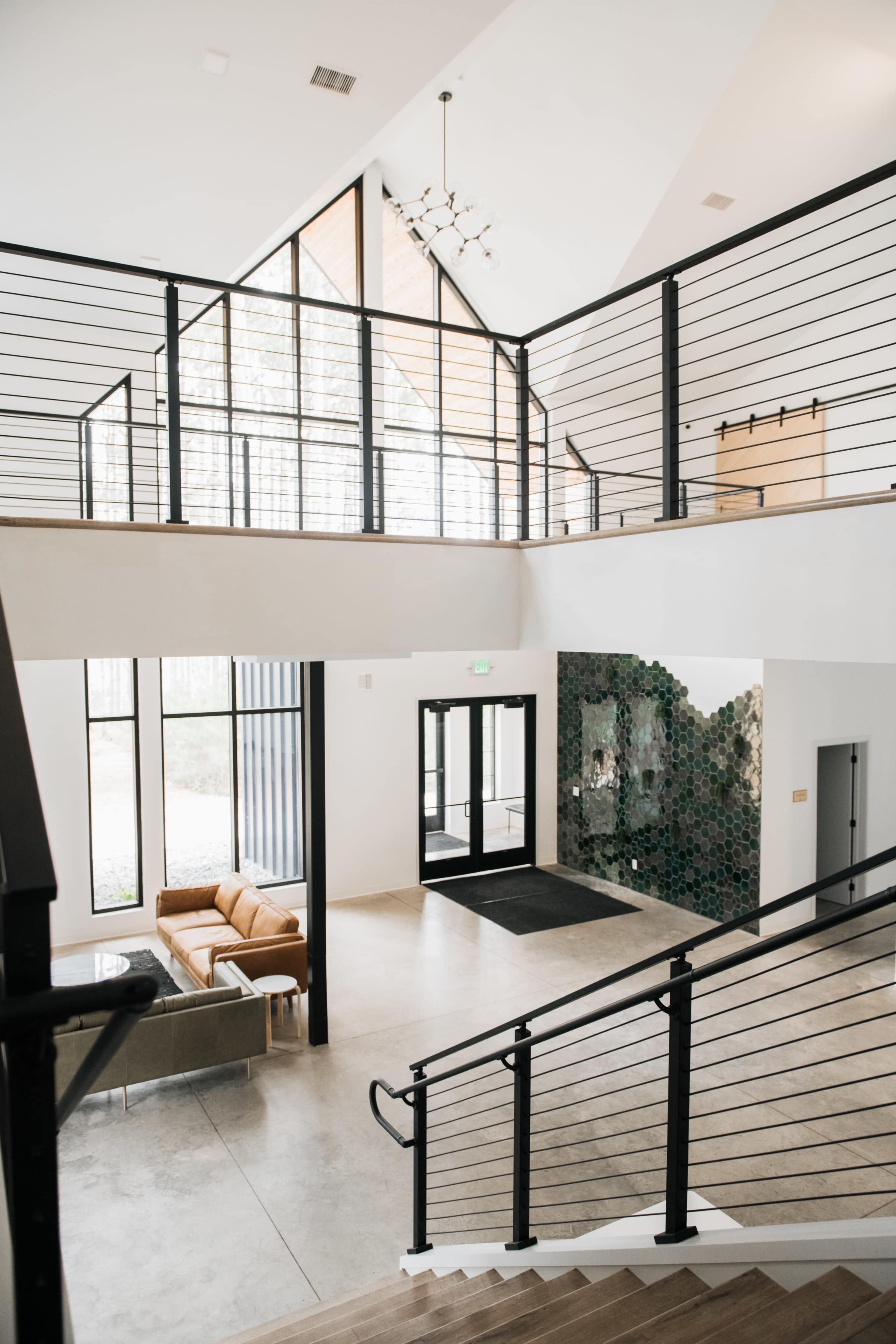 A modern entrance hall with a staircase, large windows, seating area, and decorative tile wall.