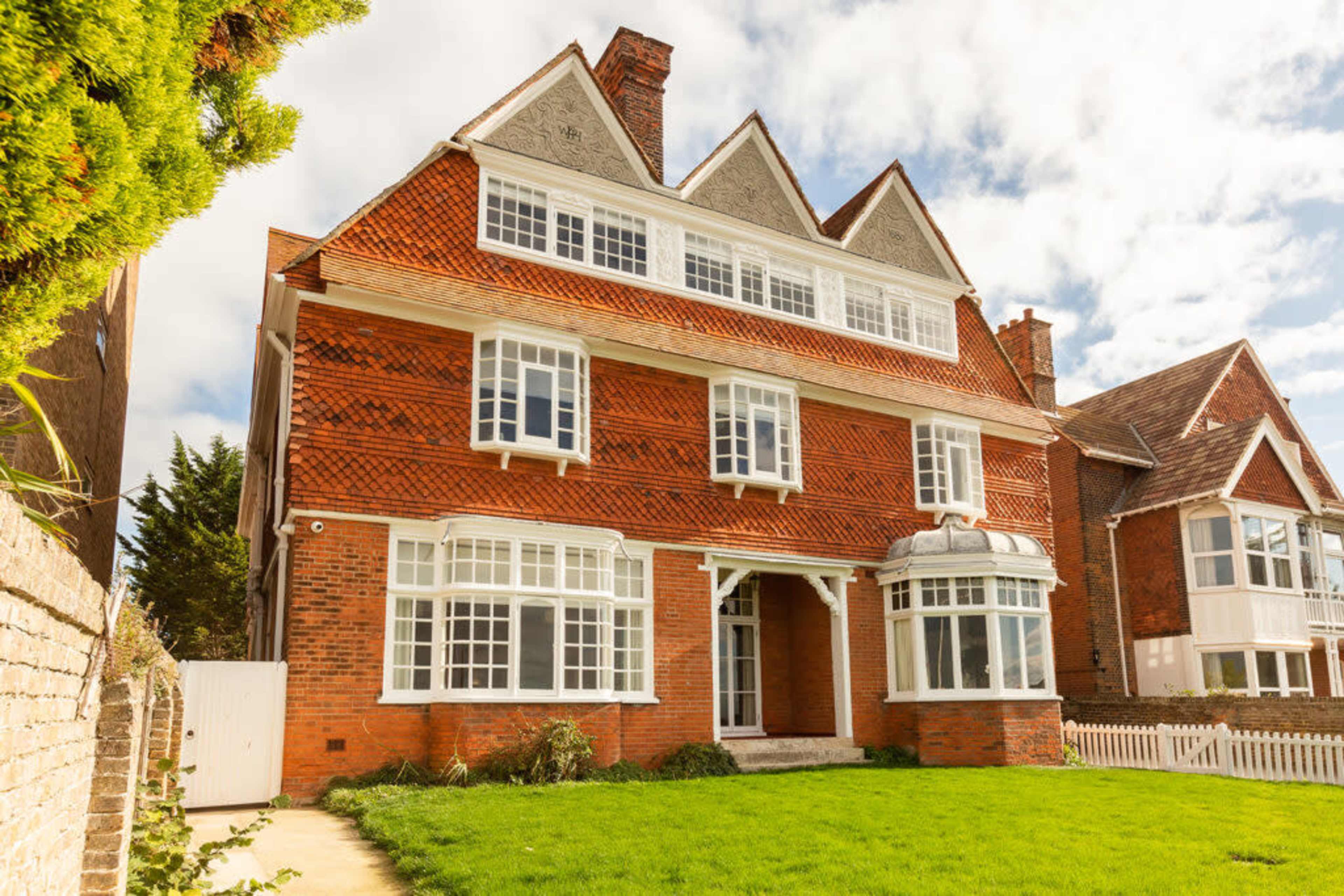 A large, three-story red brick house with multiple gabled roofs and a front lawn.