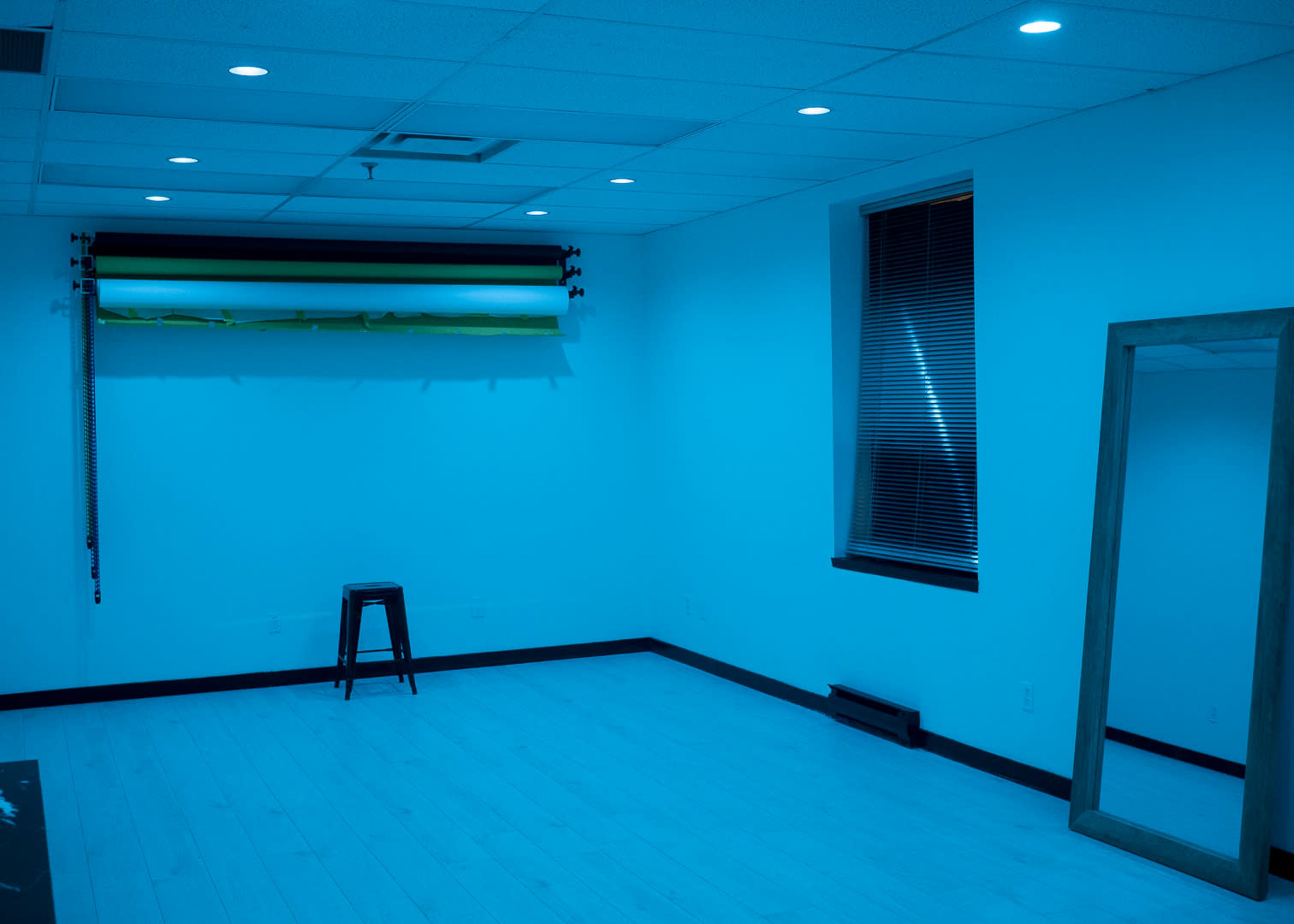 The room contains a stool, a large mirror, and a backdrop mounted on the wall, all illuminated by blue light.