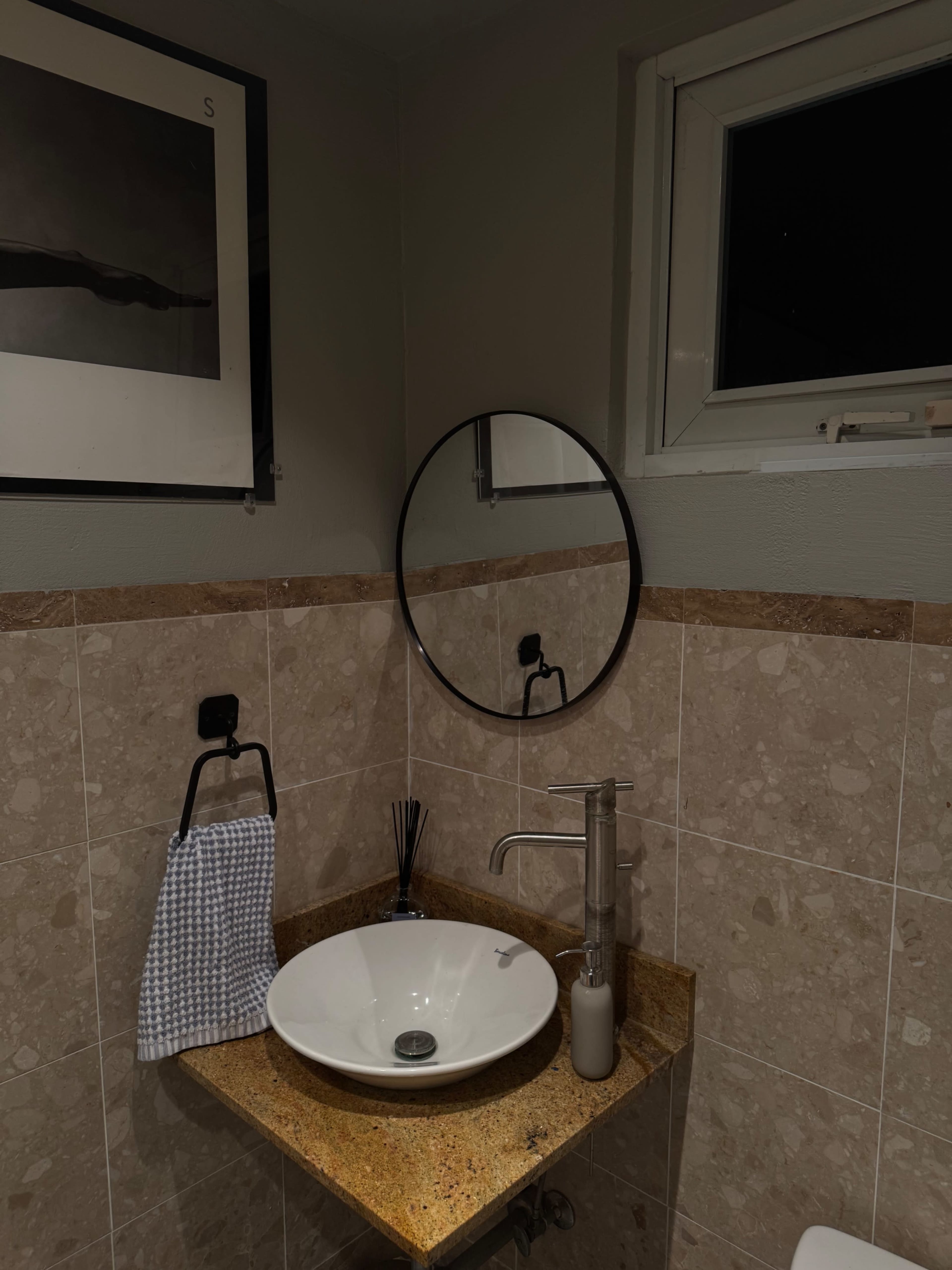 The image shows a modern bathroom sink area with a round mirror, a soap dispenser, and a decorative towel on the counter.