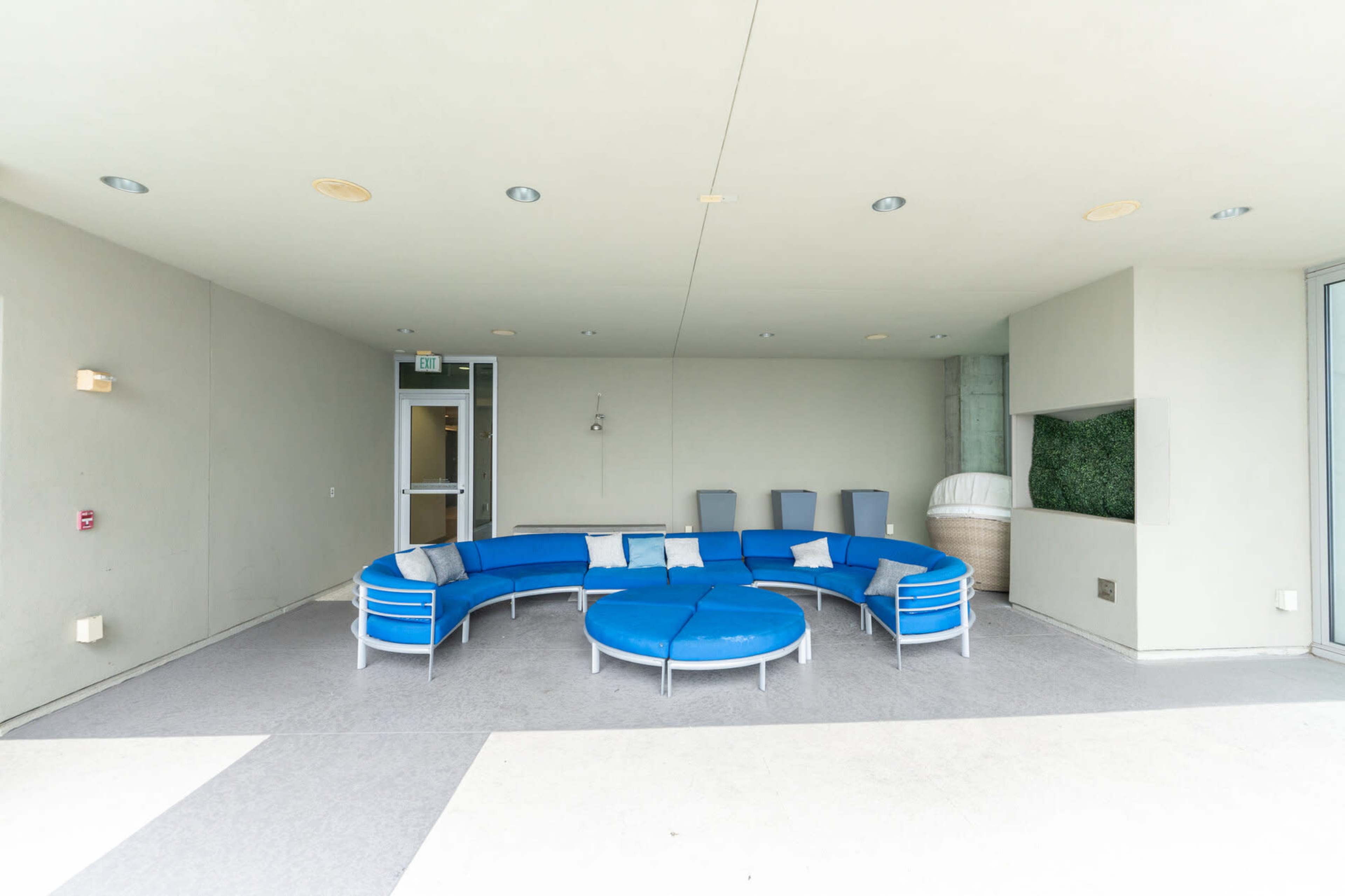 The image shows a circular seating arrangement with blue cushions situated in a minimalist, indoor space.