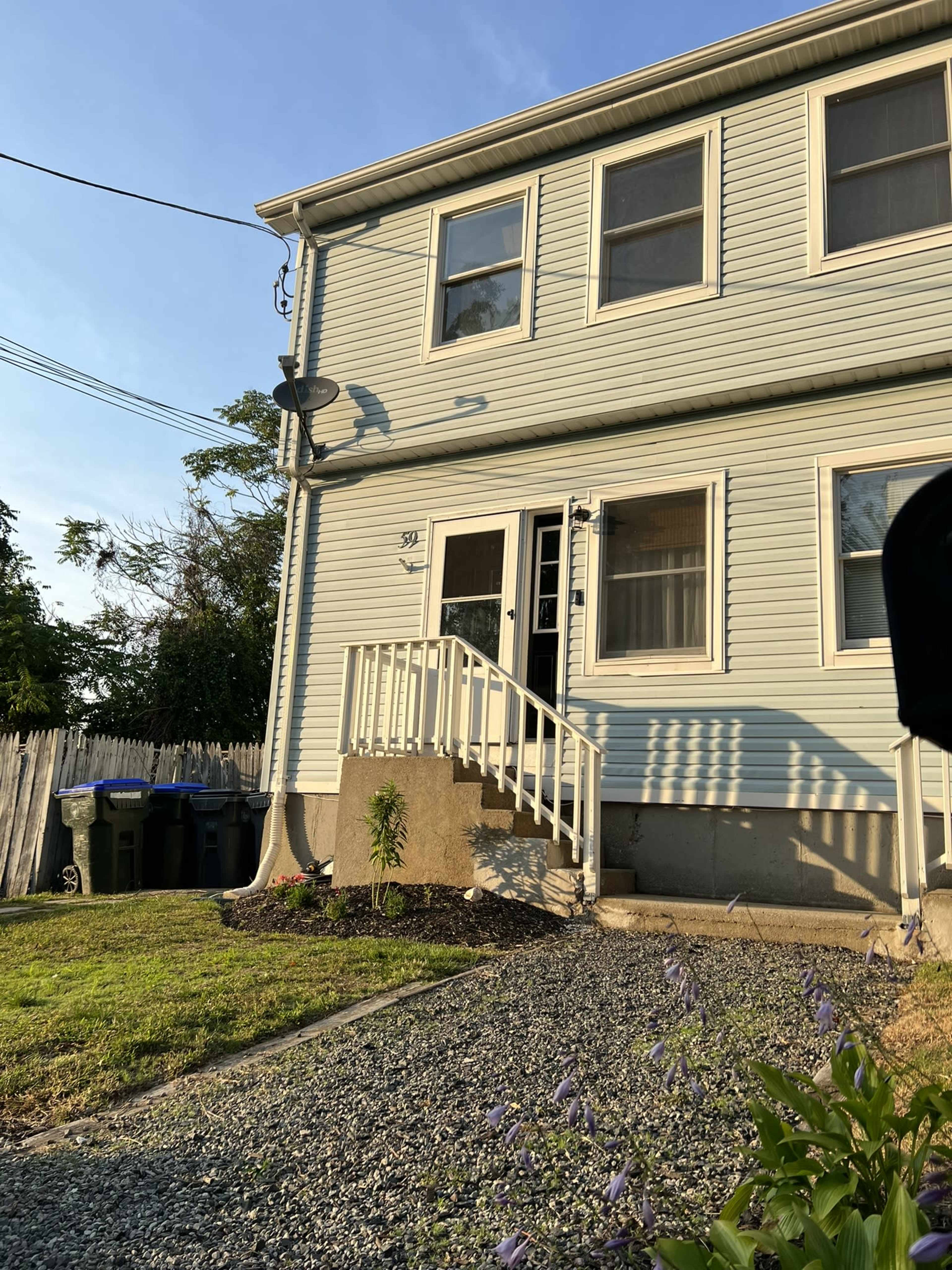 A light blue two-story house with a white railing staircase and a gravel front yard.