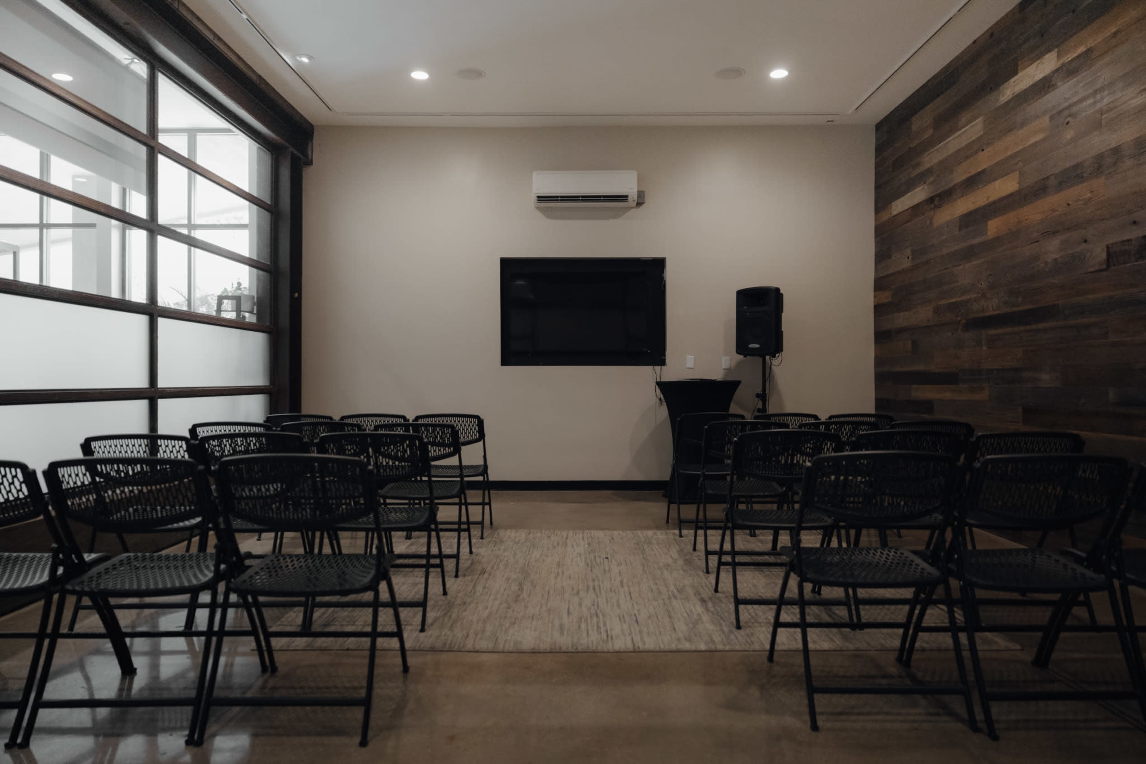 A meeting room is set up with rows of black chairs facing a wall-mounted TV and a speaker.