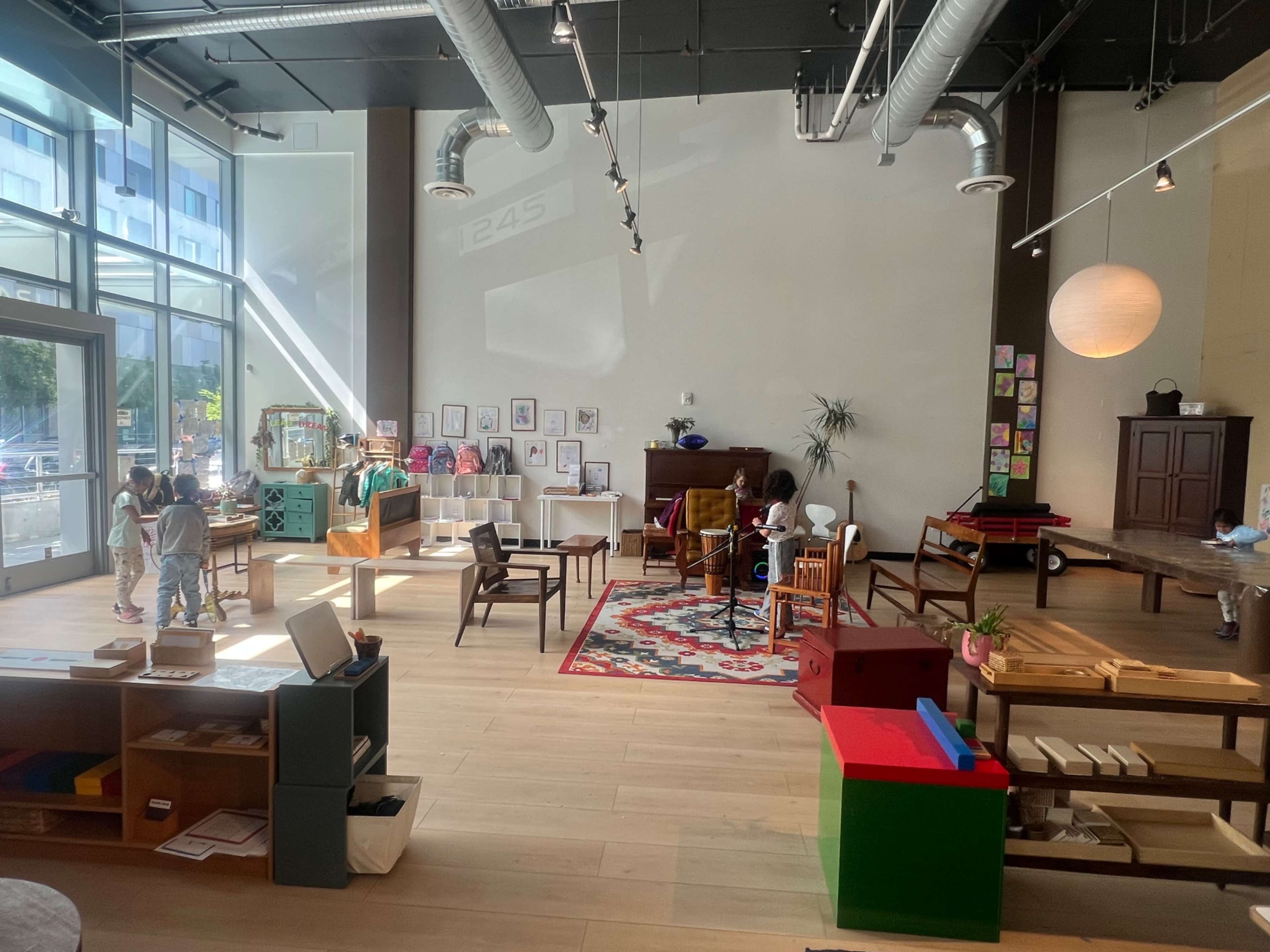 The image shows a spacious indoor play area filled with various pieces of furniture and educational toys, where children are engaged in different activities.