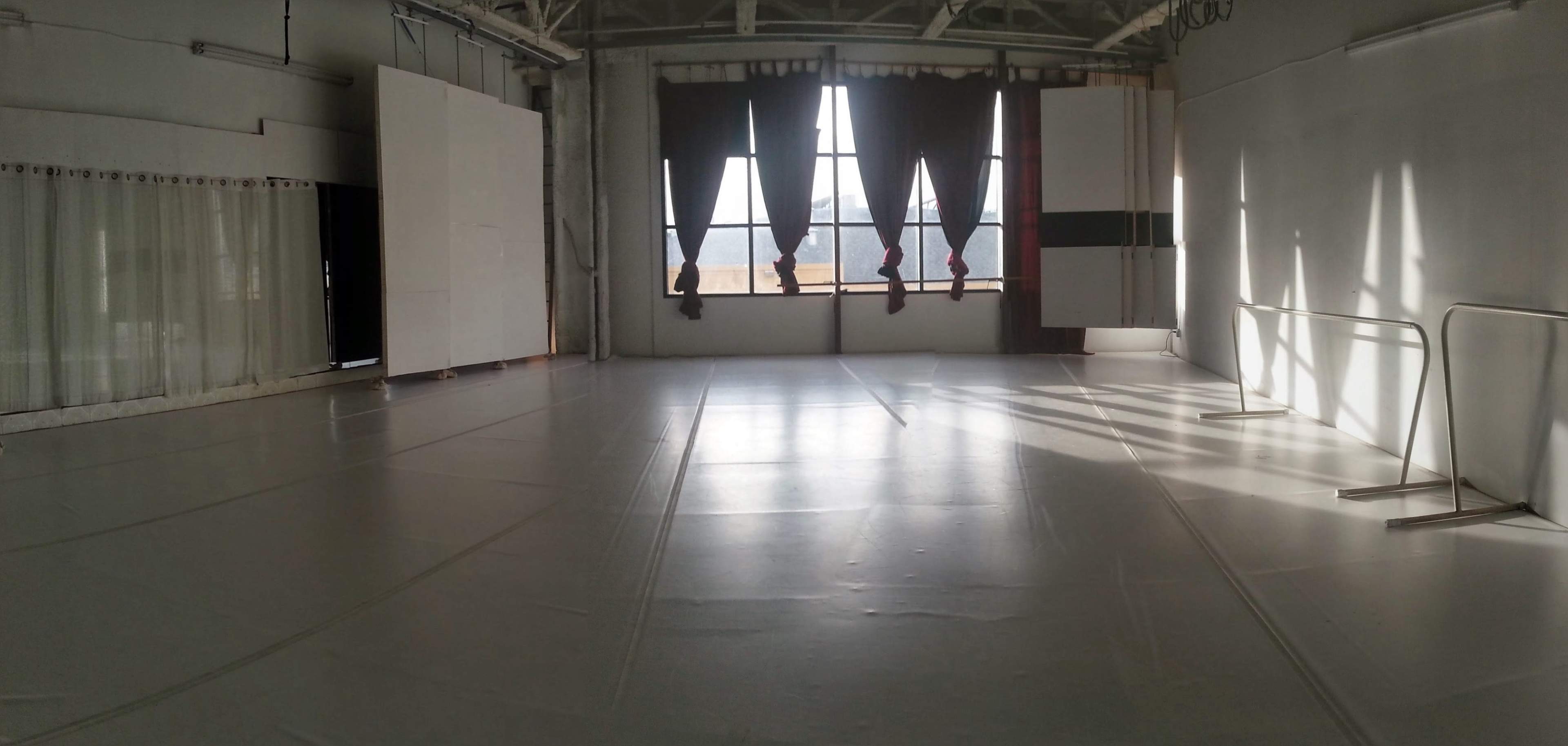 A spacious dance studio with large windows, sunlight streaming in, and a mirrored wall.
