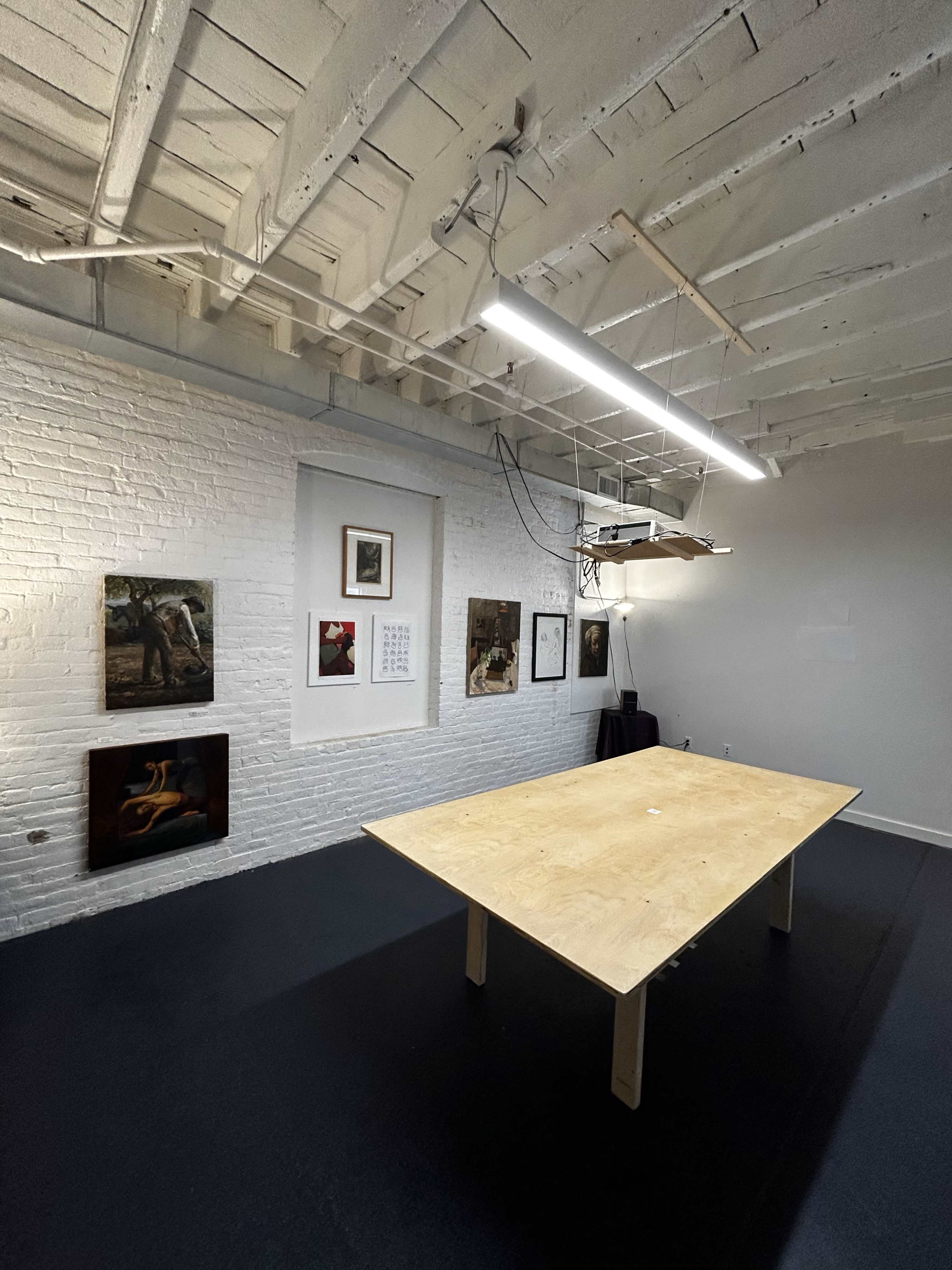 A simple wooden table is centered in a room with white brick walls adorned with various framed artworks.