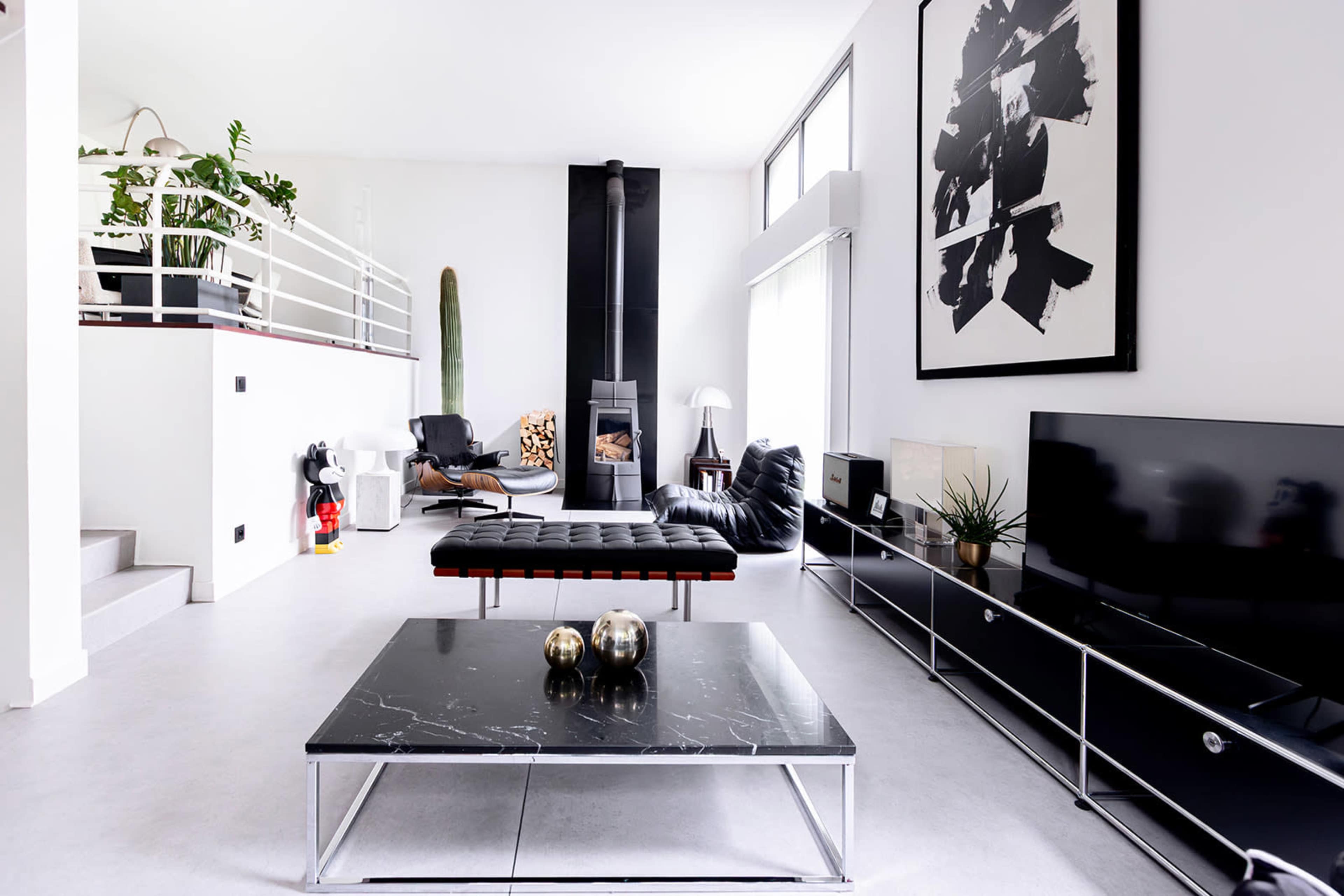 A modern living room featuring a large black coffee table, a sleek television stand, and a minimalist fireplace, with stylish furniture and indoor plants.