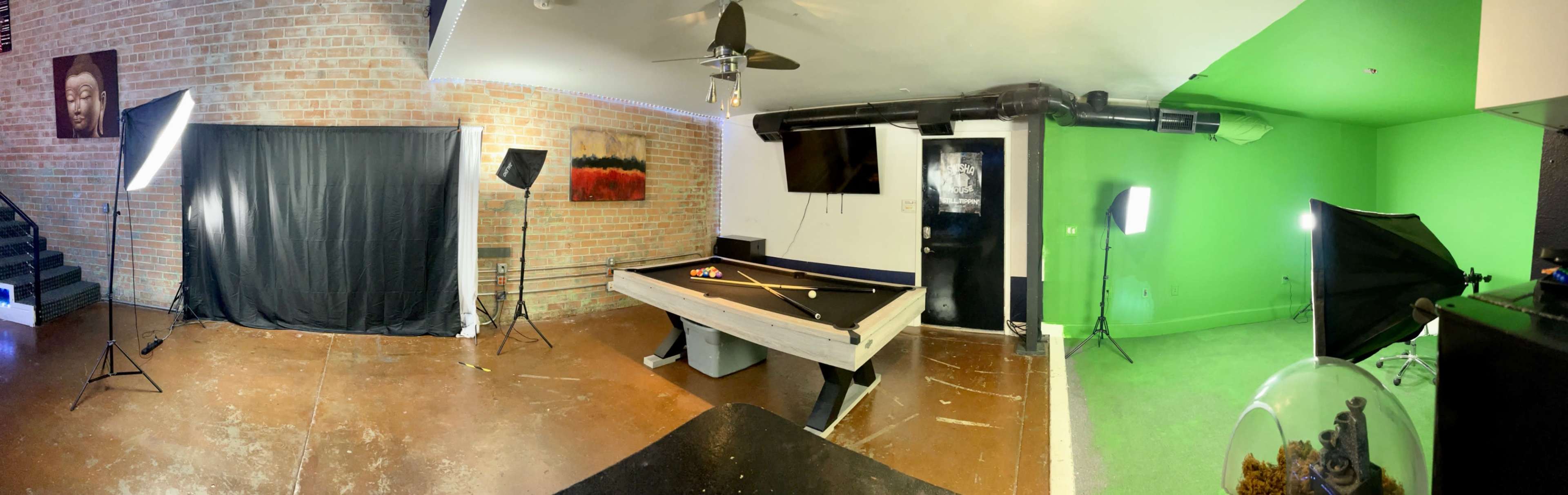 A spacious room featuring a pool table, photography lighting setups, and a green screen on one wall.