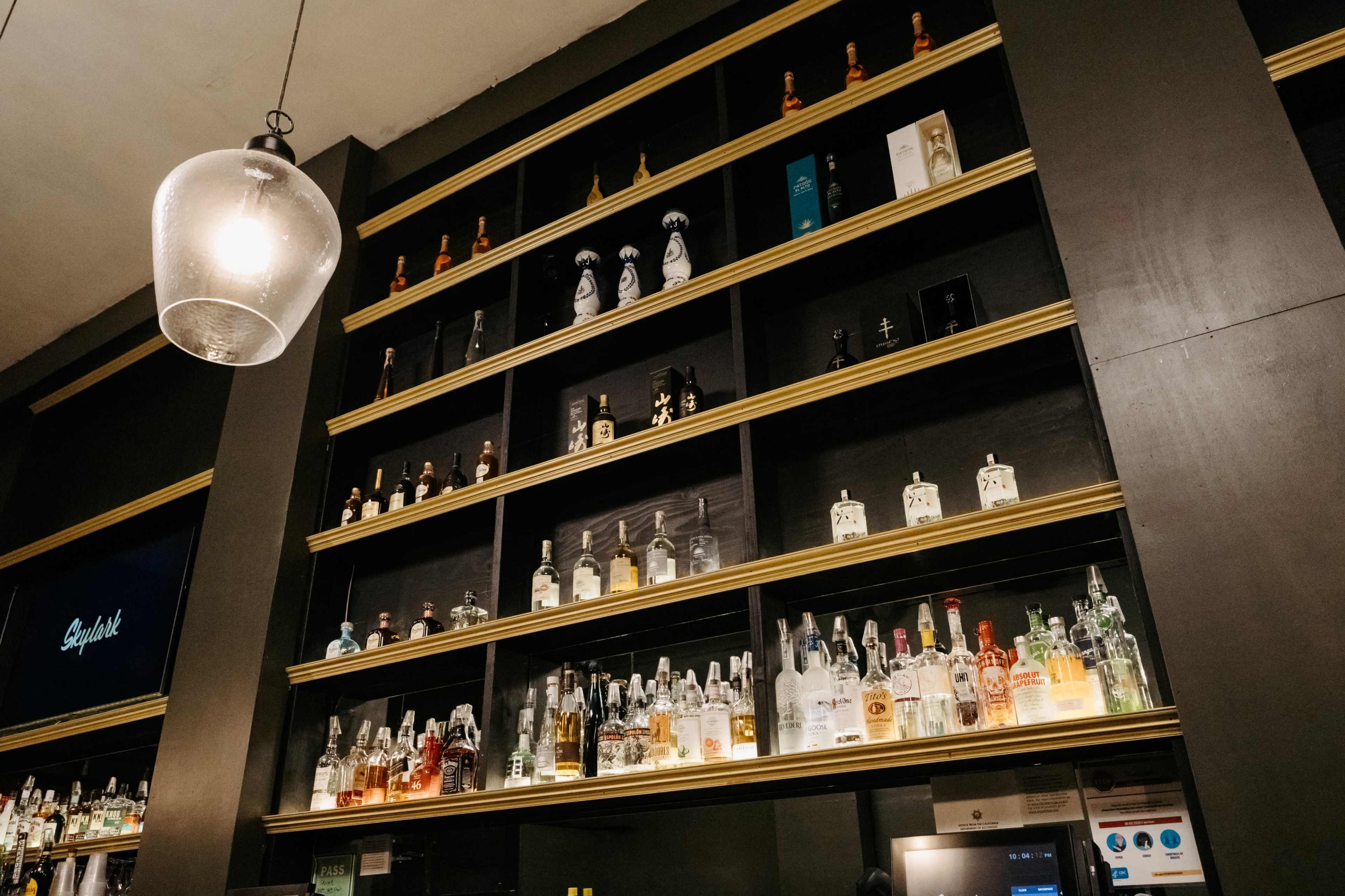 The image shows a bar shelf filled with various bottles of liquor arranged neatly on multiple tiers.