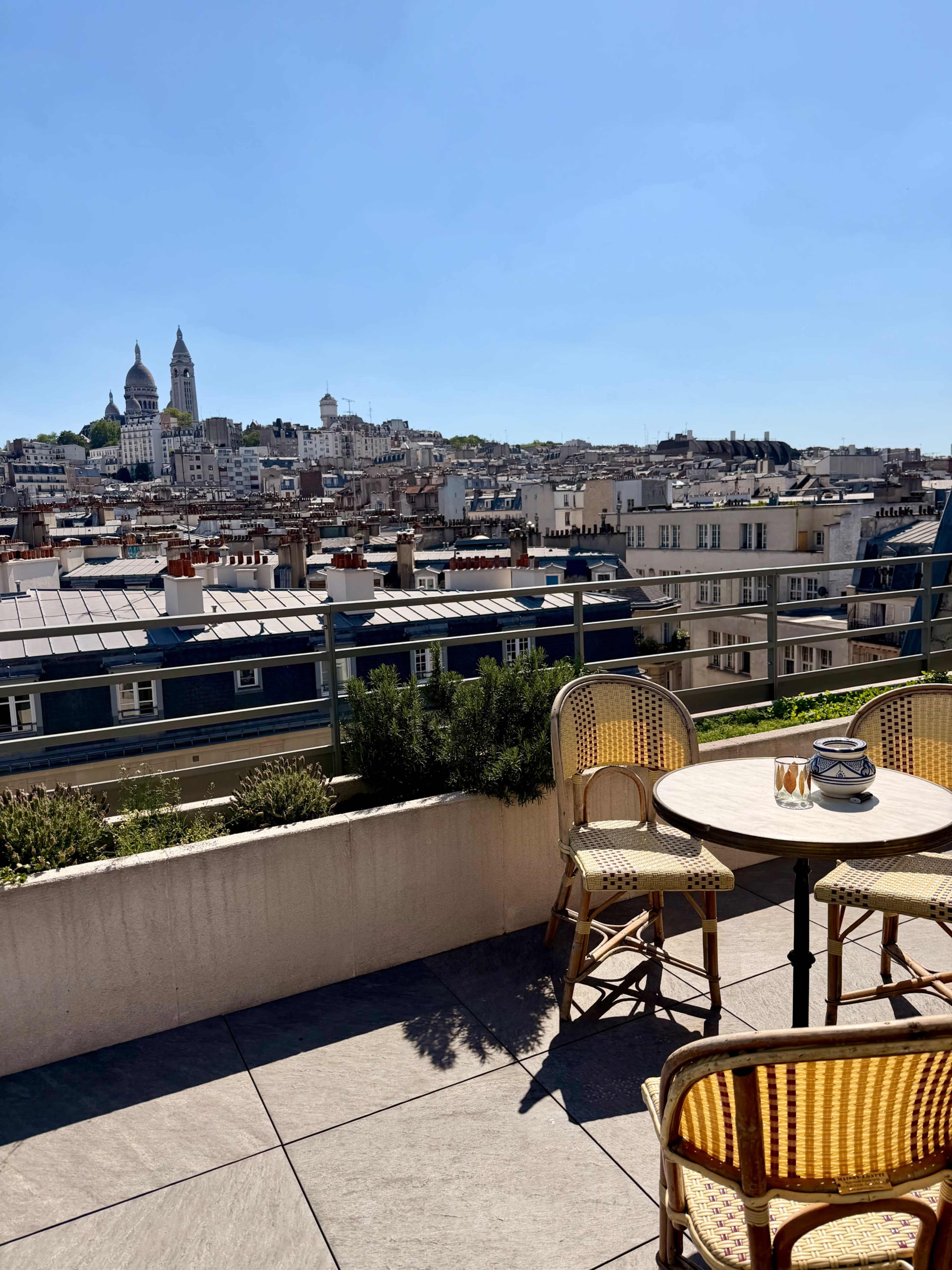 A terrace with a round table and chairs overlooks a cityscape featuring a prominent church and a clear blue sky.