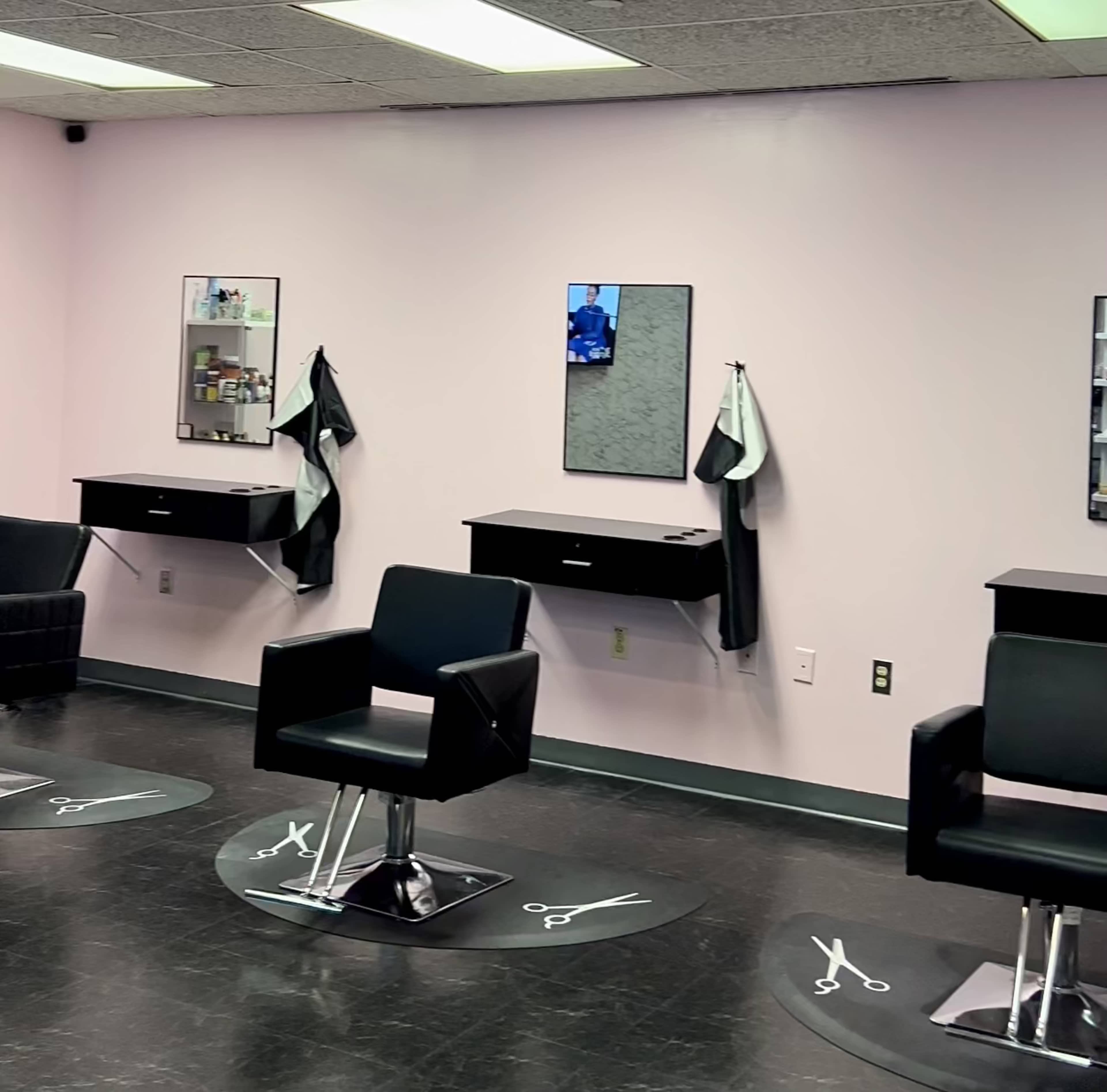 A hair salon with four black salon chairs arranged in front of mirrors on light pink walls.