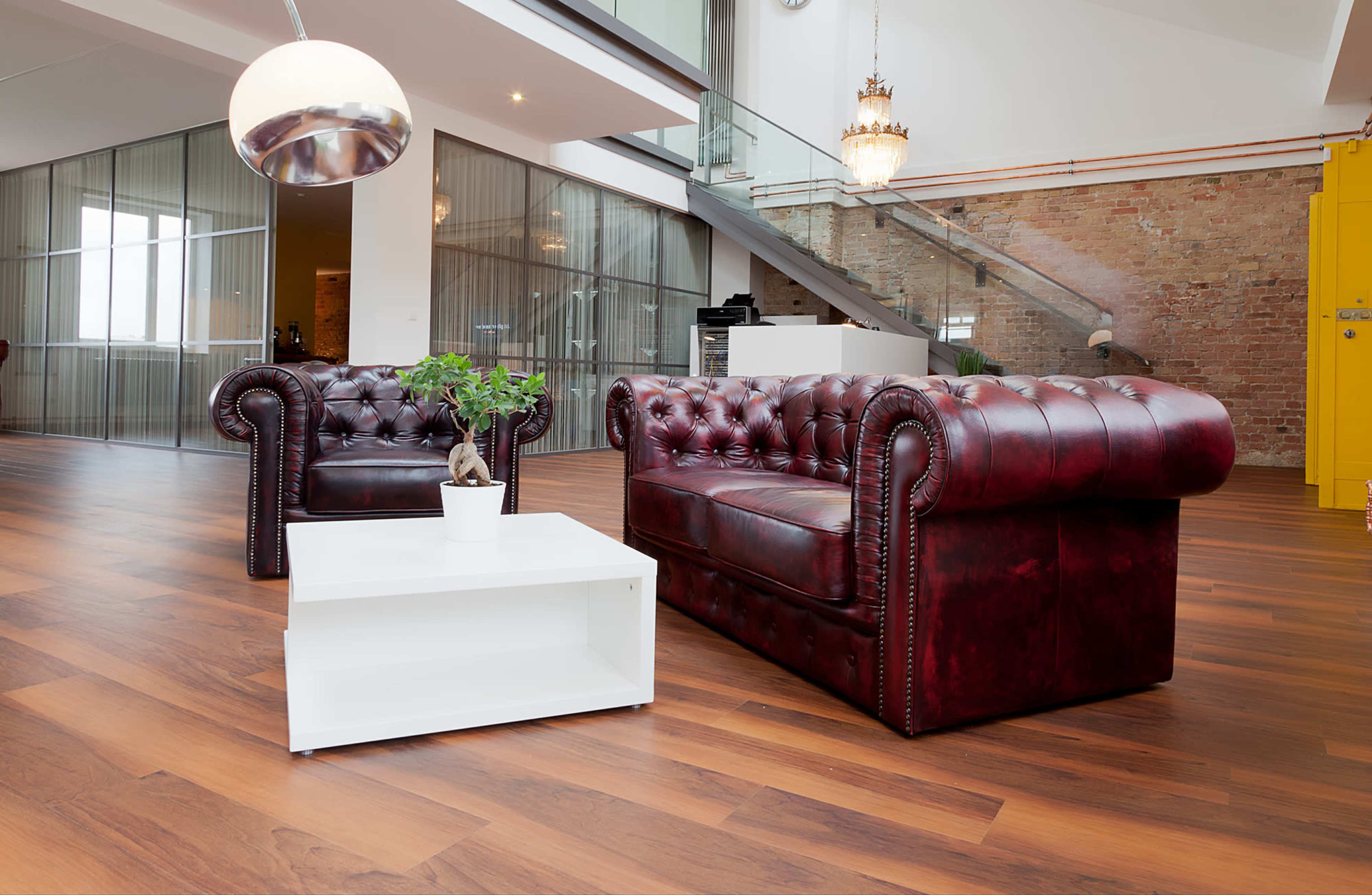 A modern, open living space with hardwood floors, featuring two burgundy leather sofas and a white coffee table.