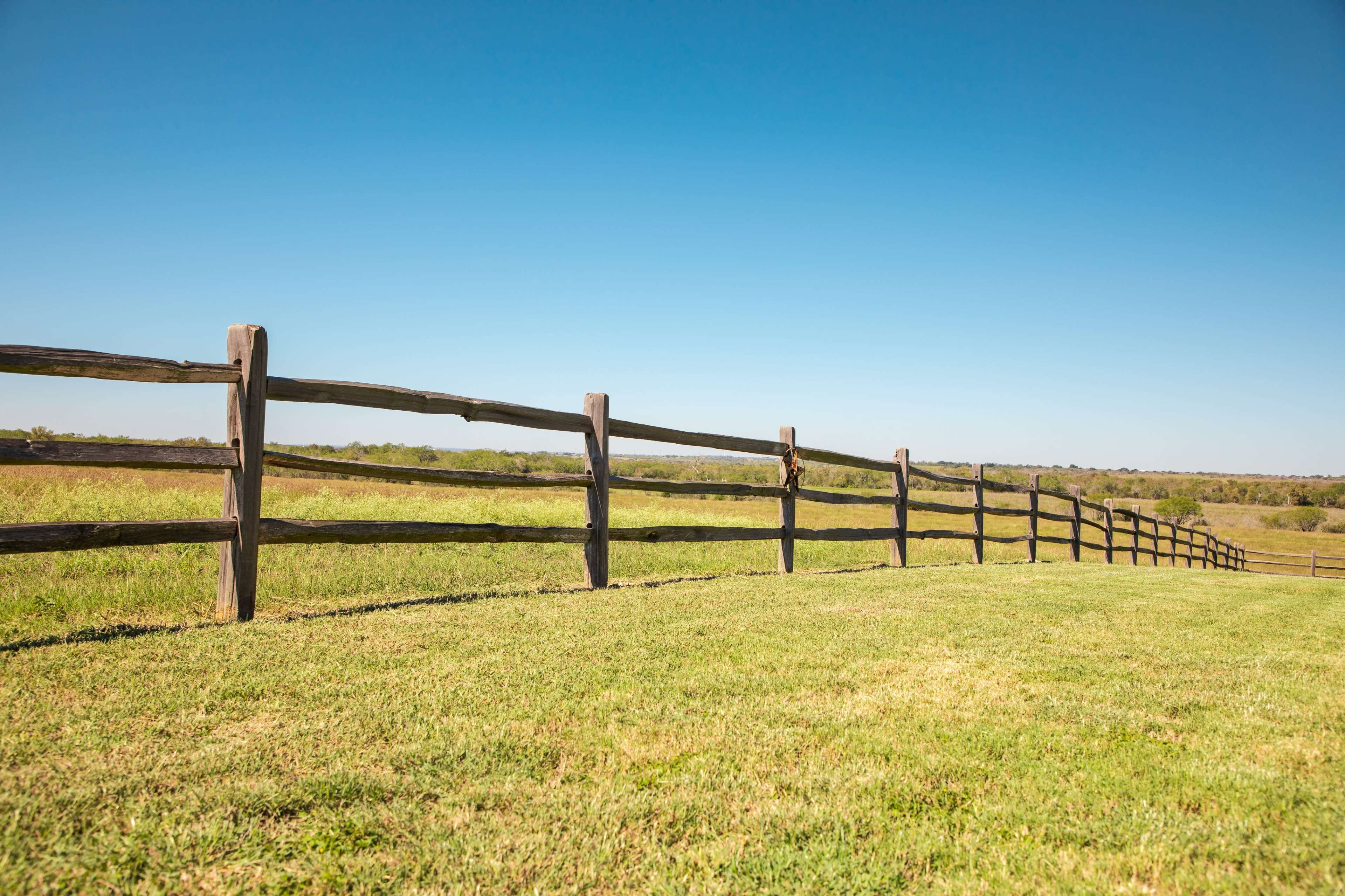 A wooden fence runs along a grassy field beneath a clear blue sky.