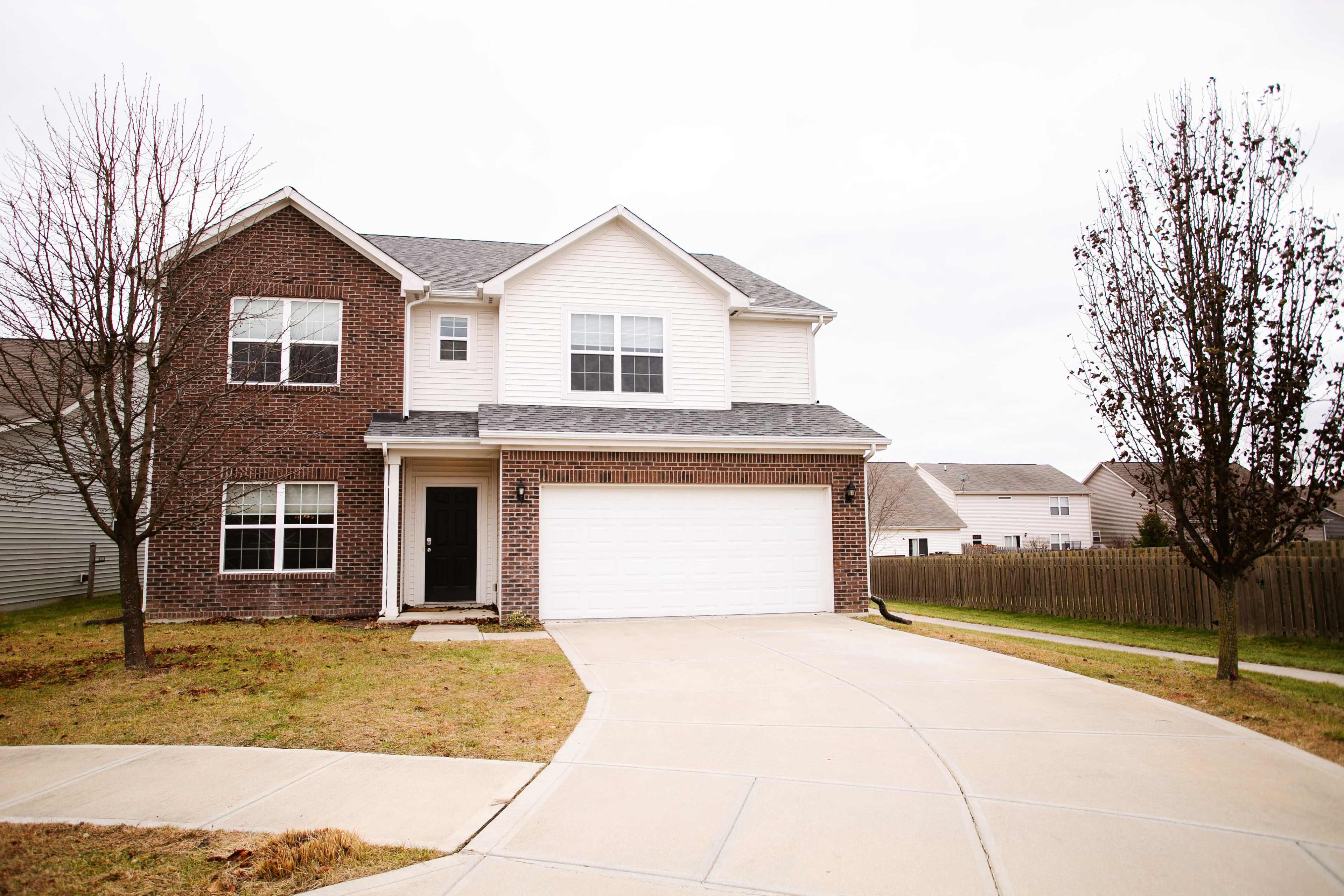 A two-story residential home with a brick facade, a large front garage, and a concrete driveway.