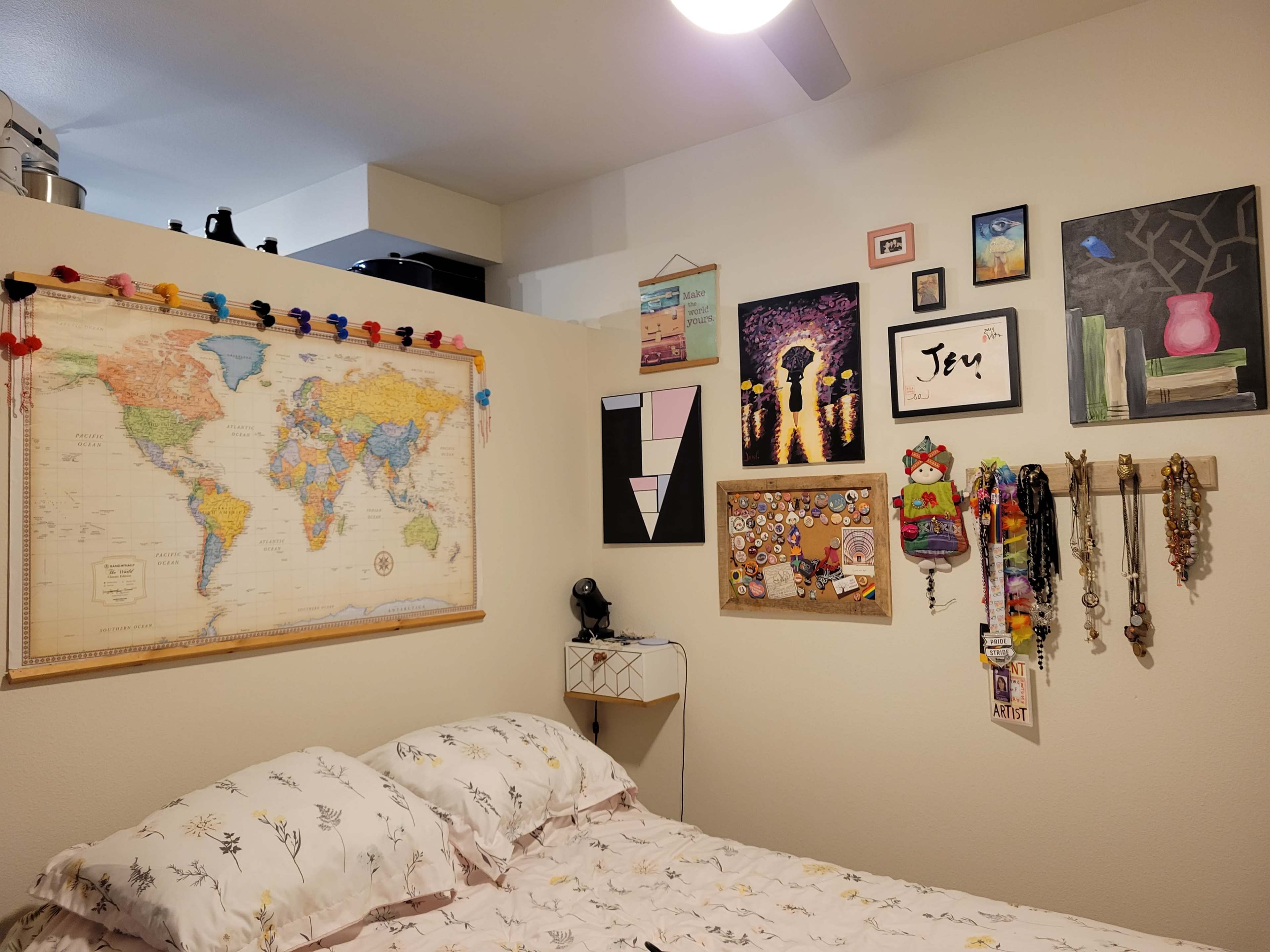 A cozy bedroom with a large world map on one wall and various framed artworks and decorations arranged around it.
