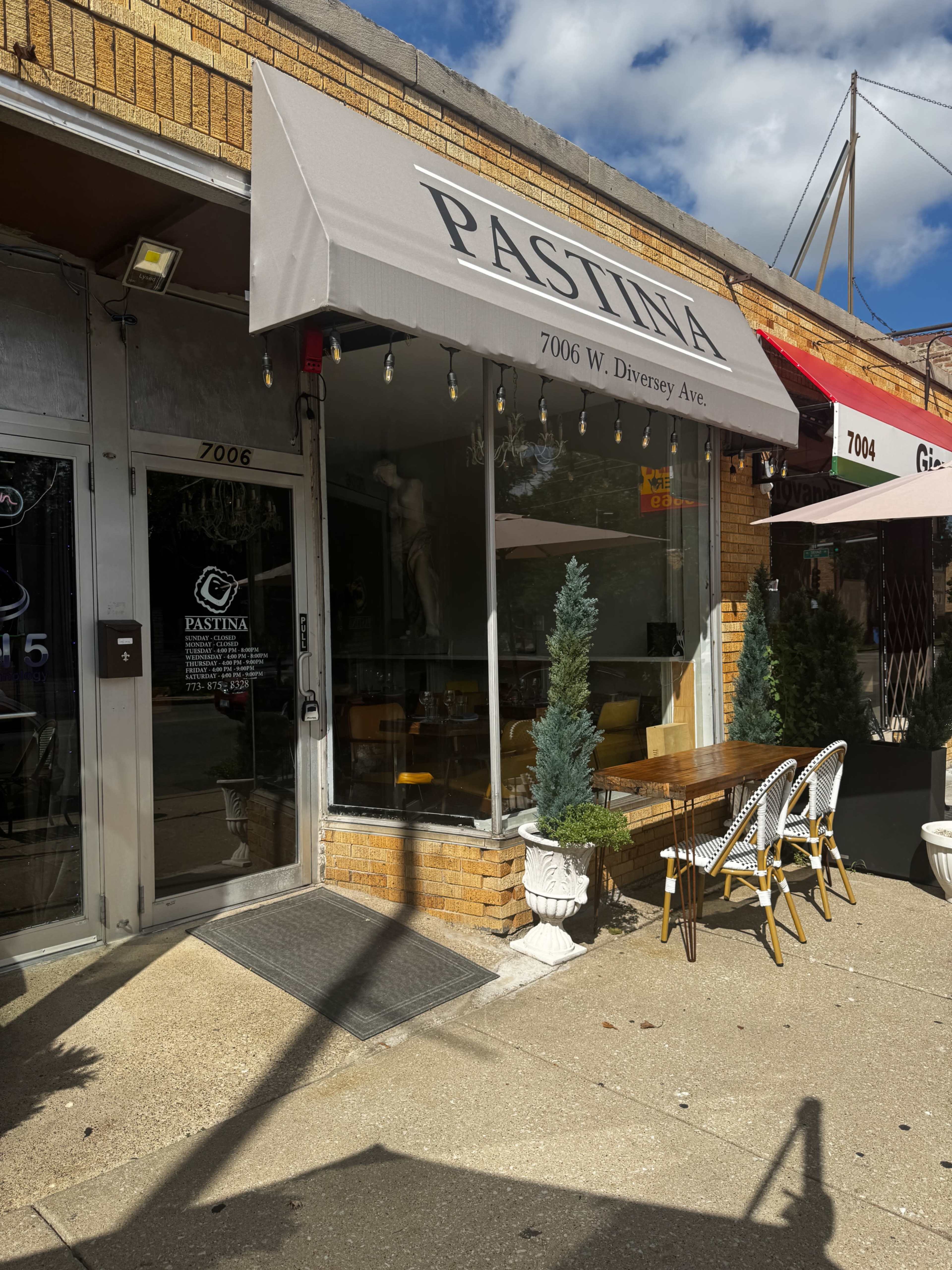 The image shows the entrance of a restaurant named Pastina, located at 7006 W. Diversey Ave, featuring outdoor seating and potted trees.