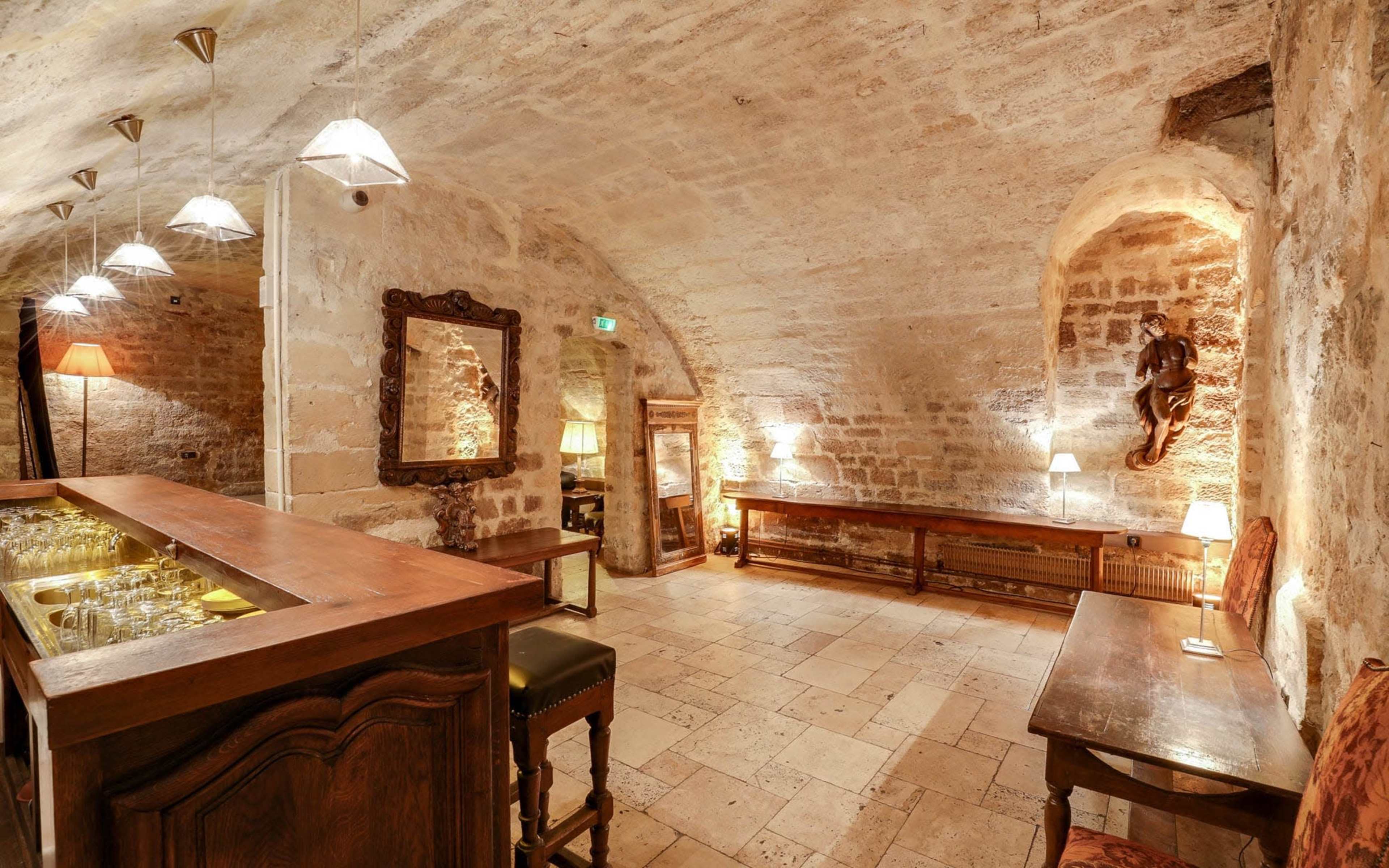 A stone-walled cellar with a bar, wooden furnishings, and various lighting fixtures.