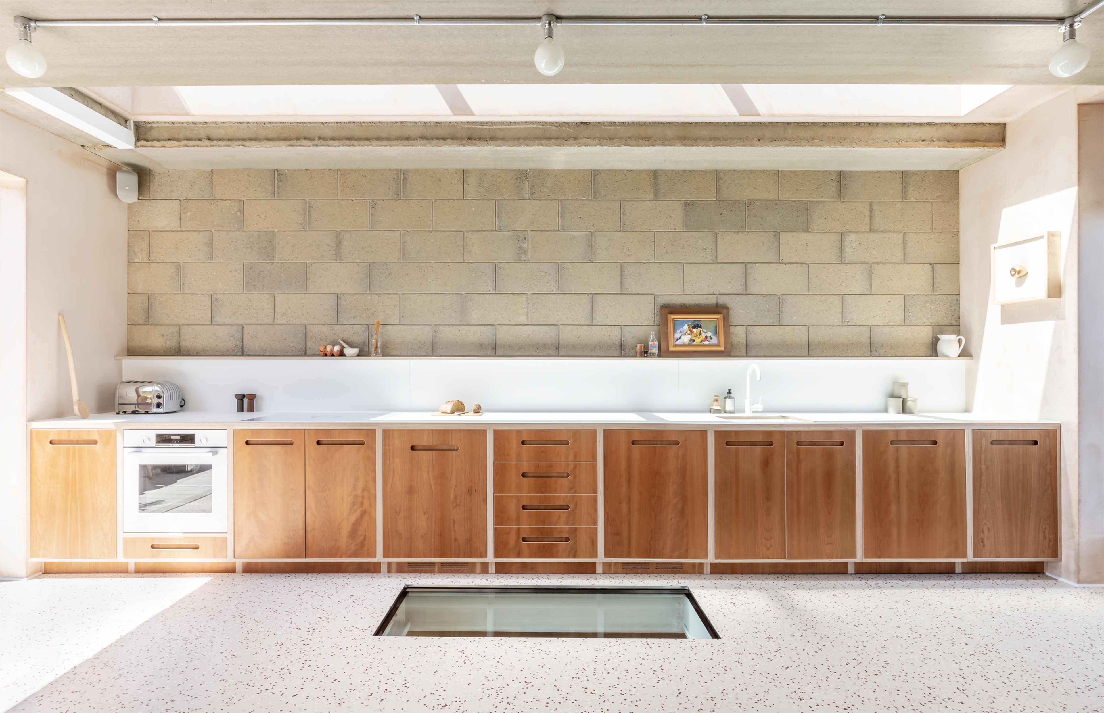 A modern kitchen features wooden cabinetry, a white countertop, and a glass section in the floor near a minimalist design.