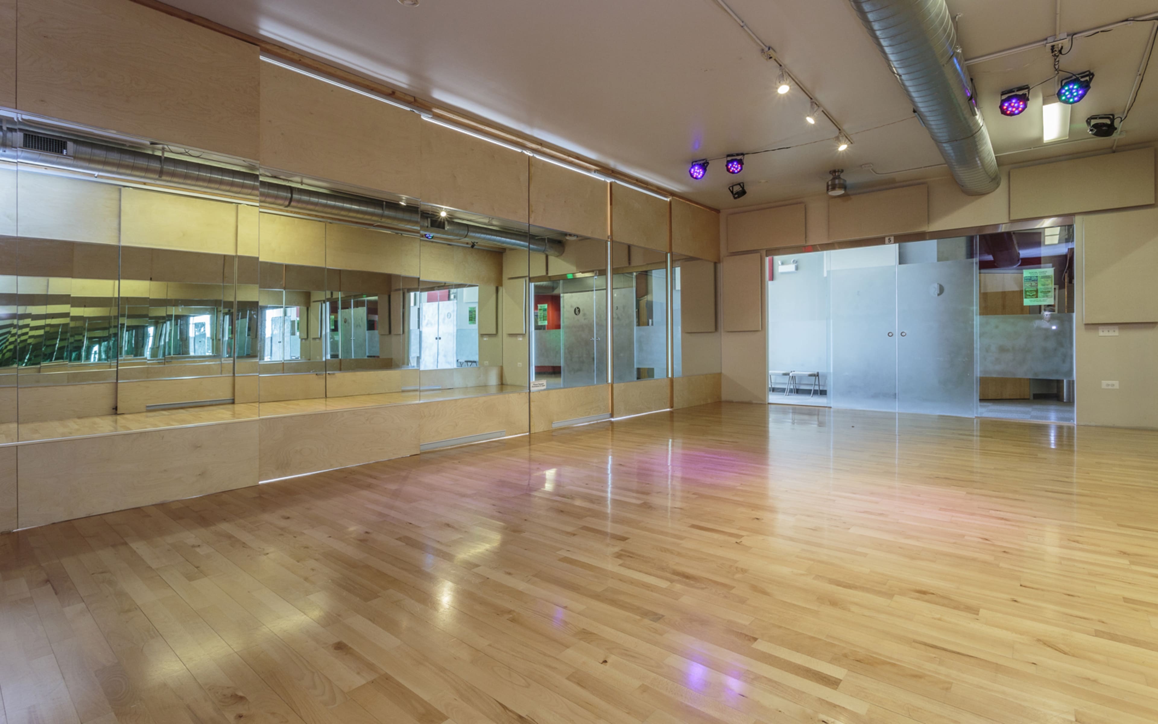 An empty dance studio with wooden floors and large mirrors across one wall.
