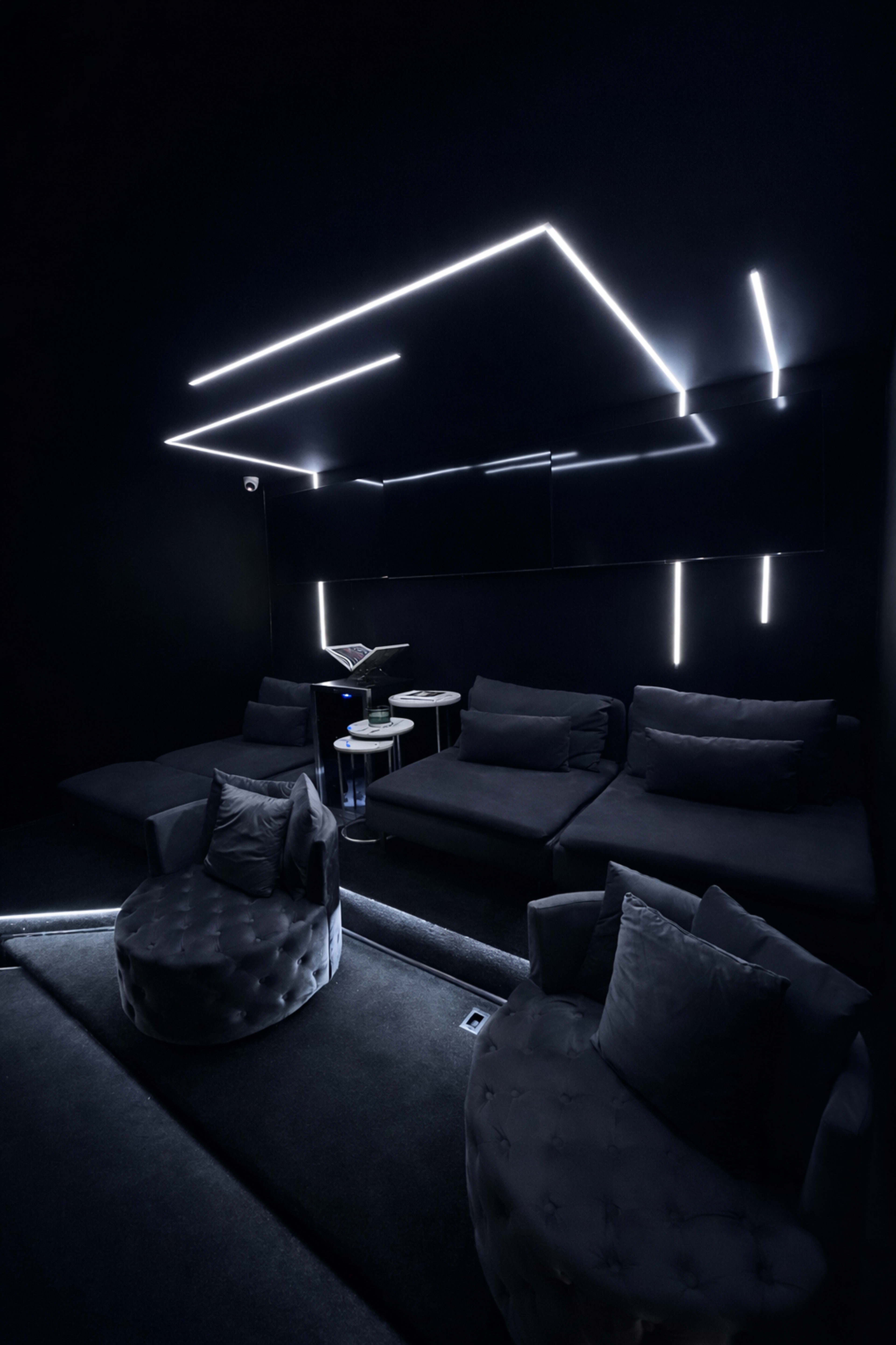 A dark room features modern seating with glowing, minimalist LED light accents on the walls and ceiling.