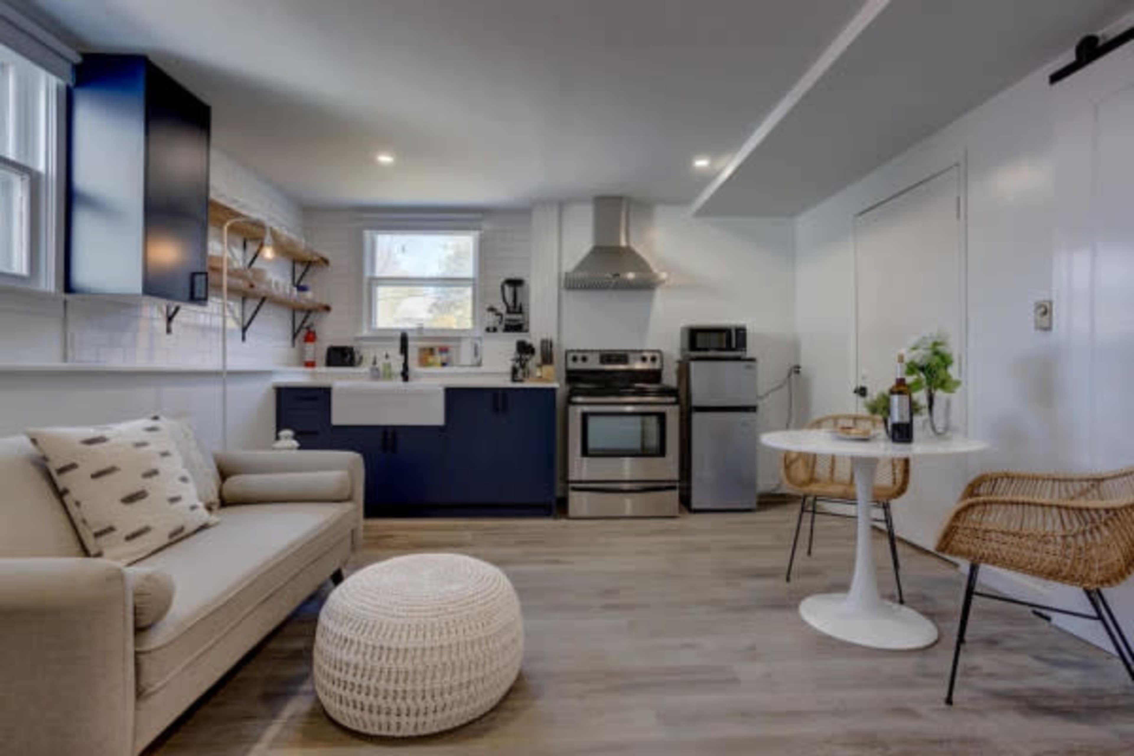 A modern kitchen features stainless steel appliances, a white sink, and a small dining table with rattan chairs.