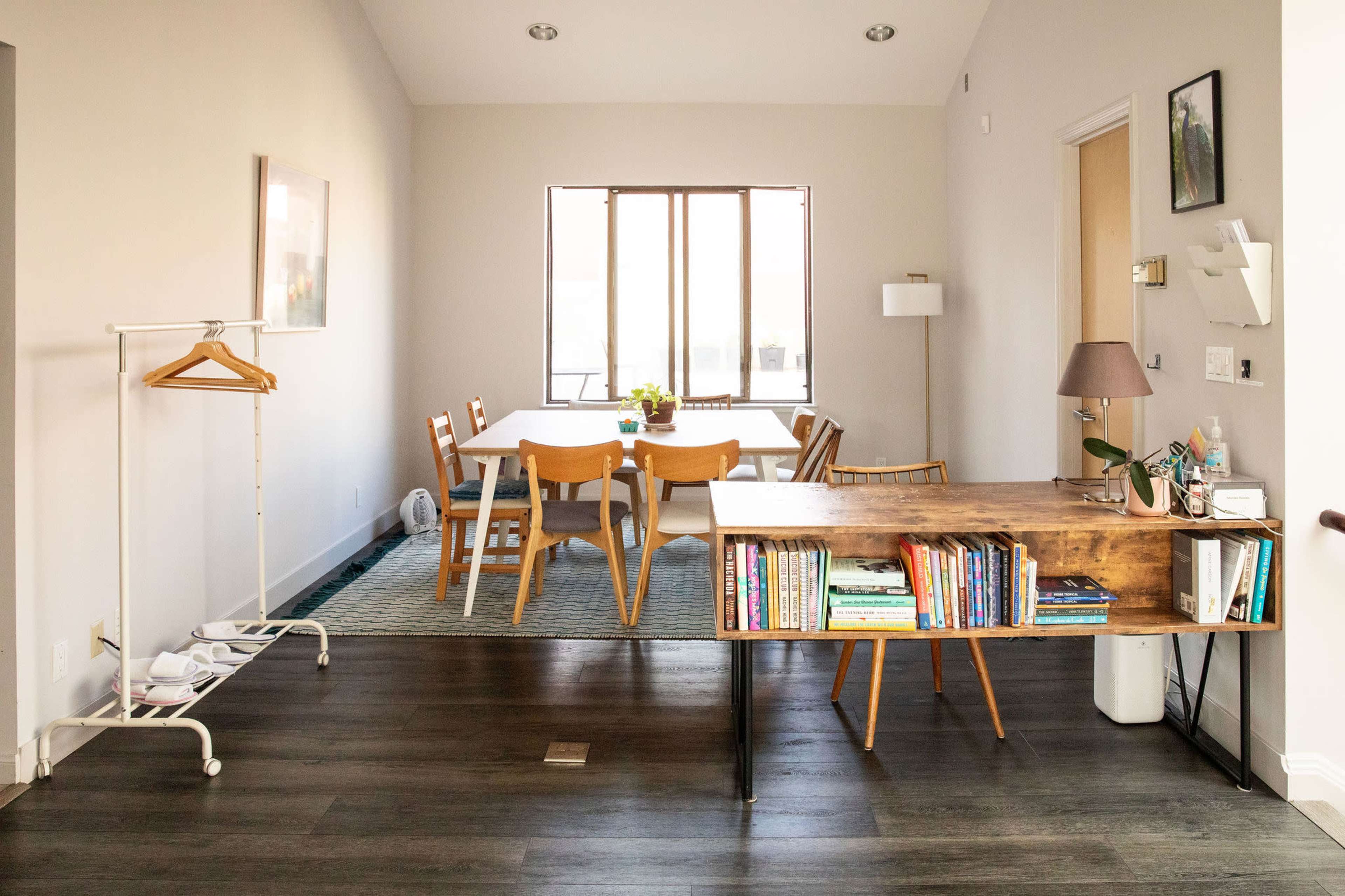 The image shows a modern, open-concept dining area with a wooden table surrounded by chairs, a bookshelf, and a coat rack.