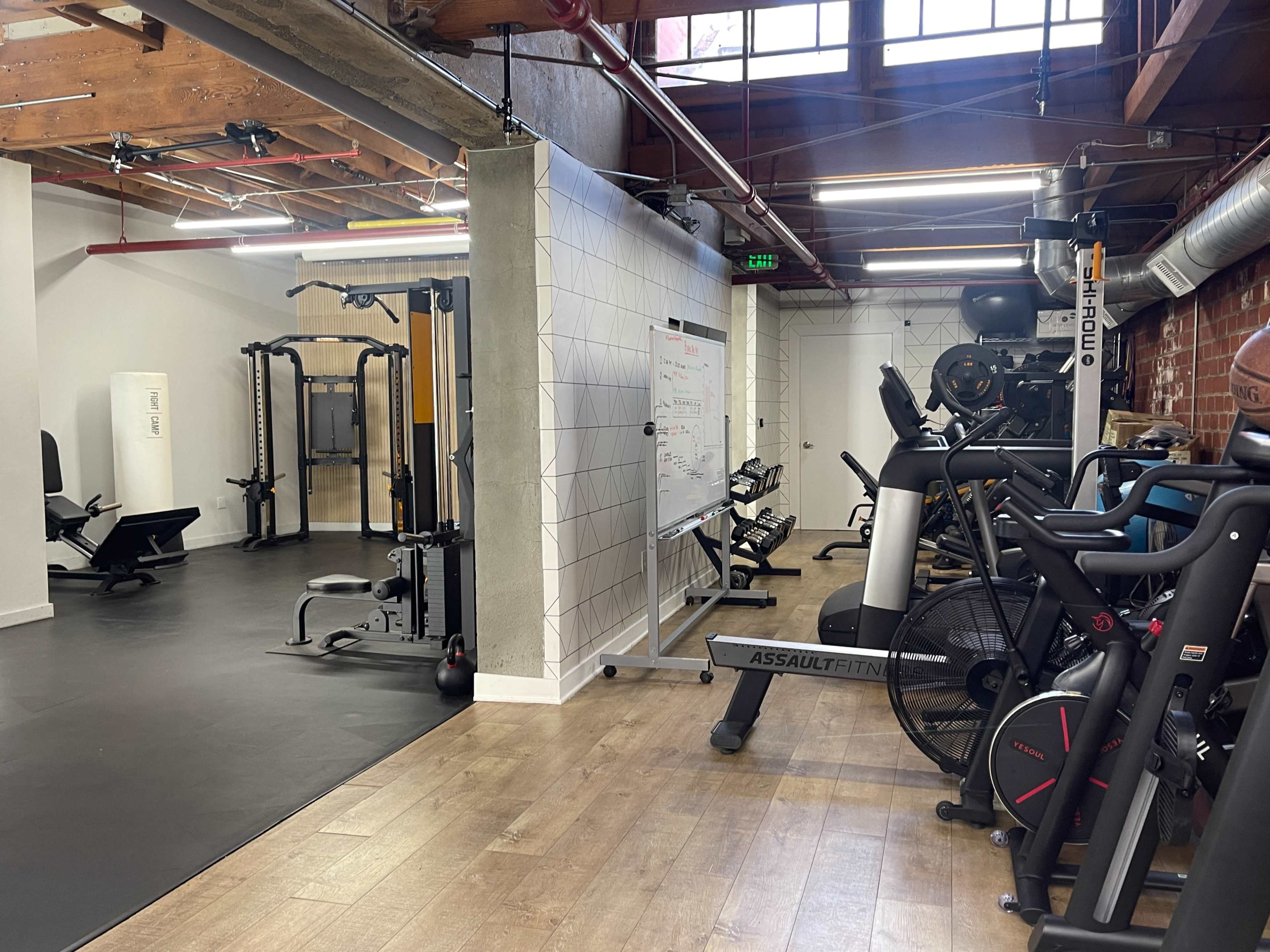 A modern gym area featuring various exercise machines, including a multi-gym, stationary bikes, and a whiteboard on the wall.