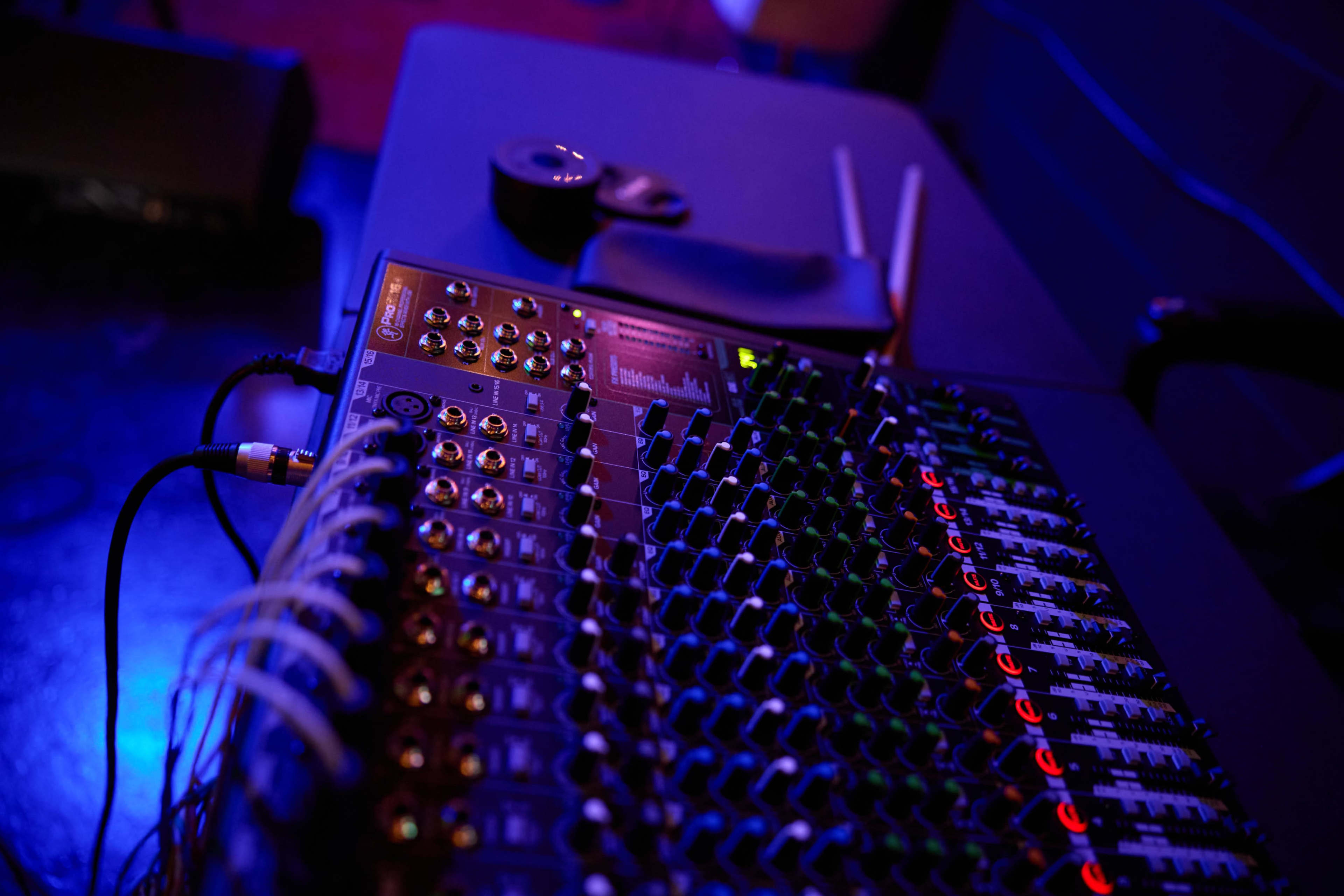 A close-up view of an audio mixing console with illuminated knobs and connections on a dark table.
