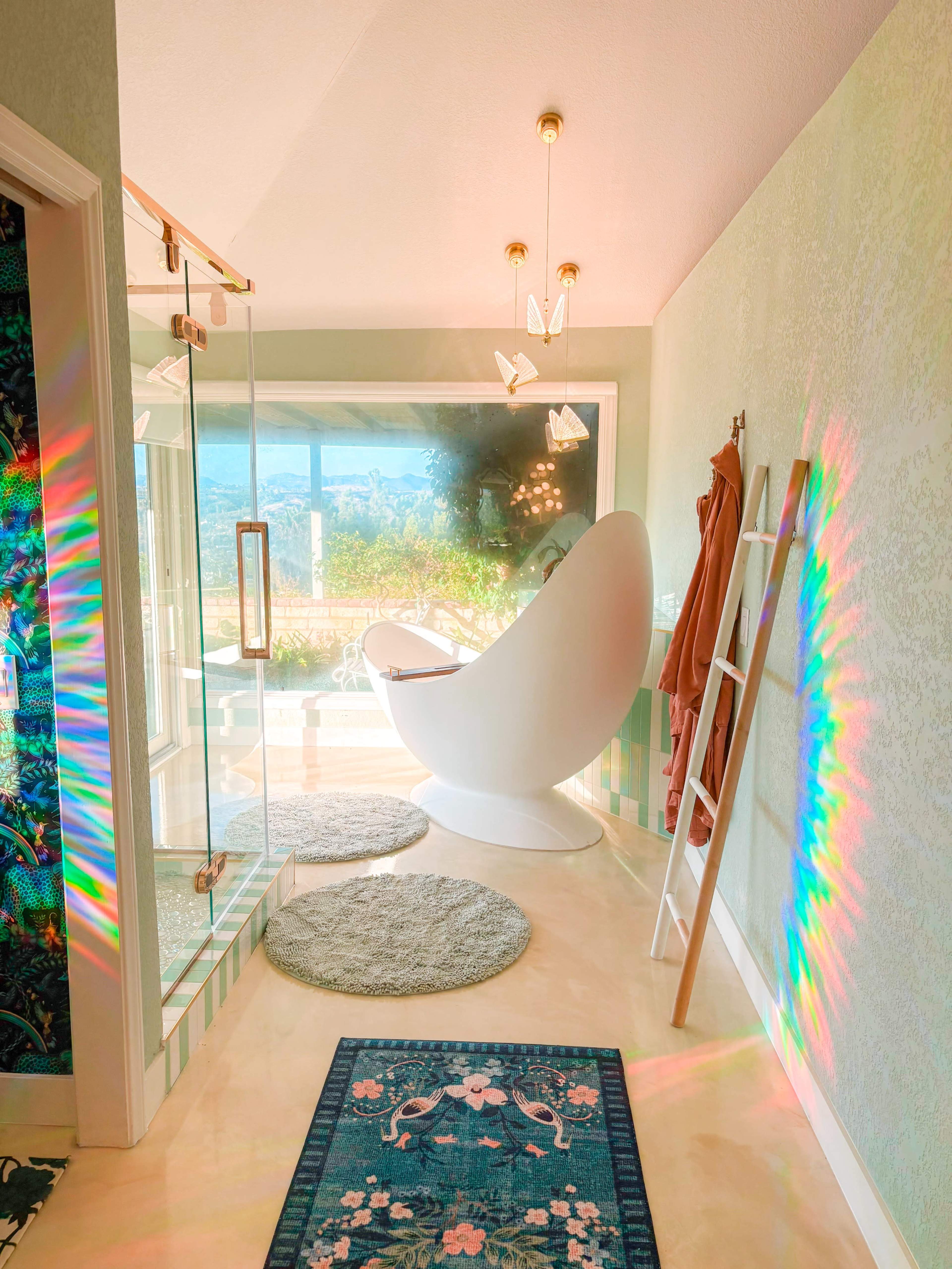 The image shows a modern bathroom featuring a freestanding white bathtub, a glass shower enclosure, and colorful light reflections on the walls.