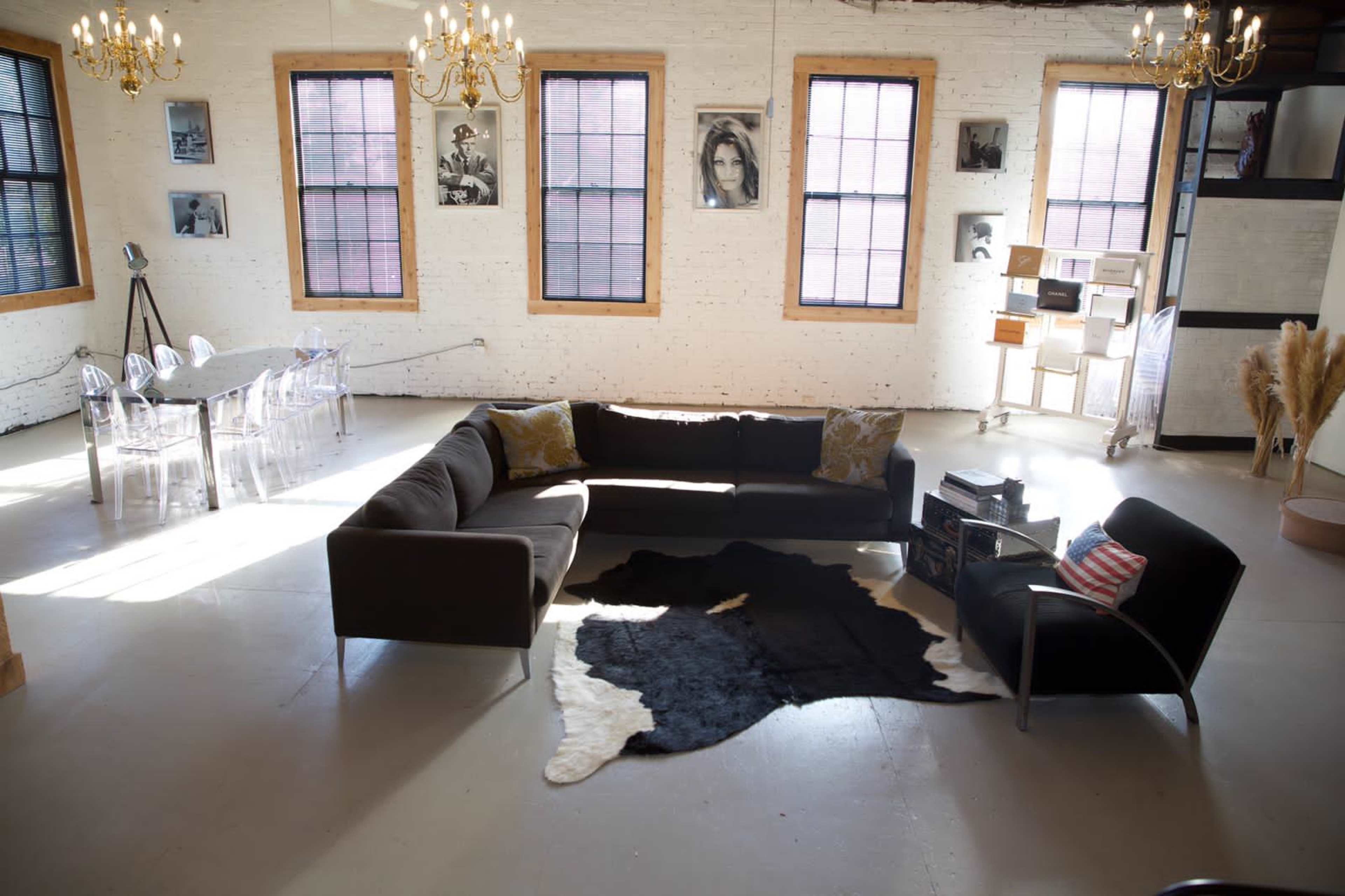 A spacious room with large windows, featuring a sectional sofa, a cowhide rug, and a dining area with clear chairs and a display shelf.