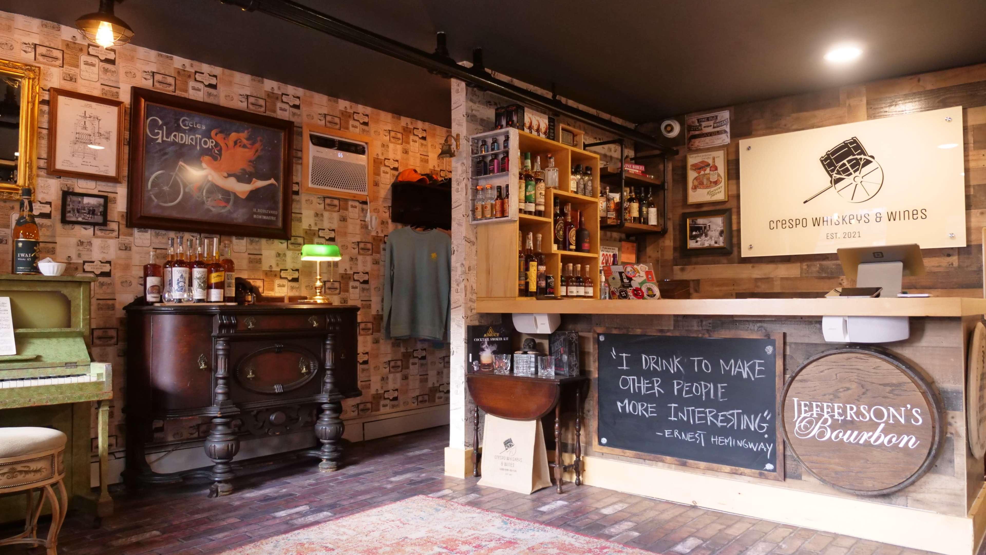 A cozy bar area featuring shelves stocked with various liquor bottles, a chalkboard with a quote, and decorative artwork on the walls.