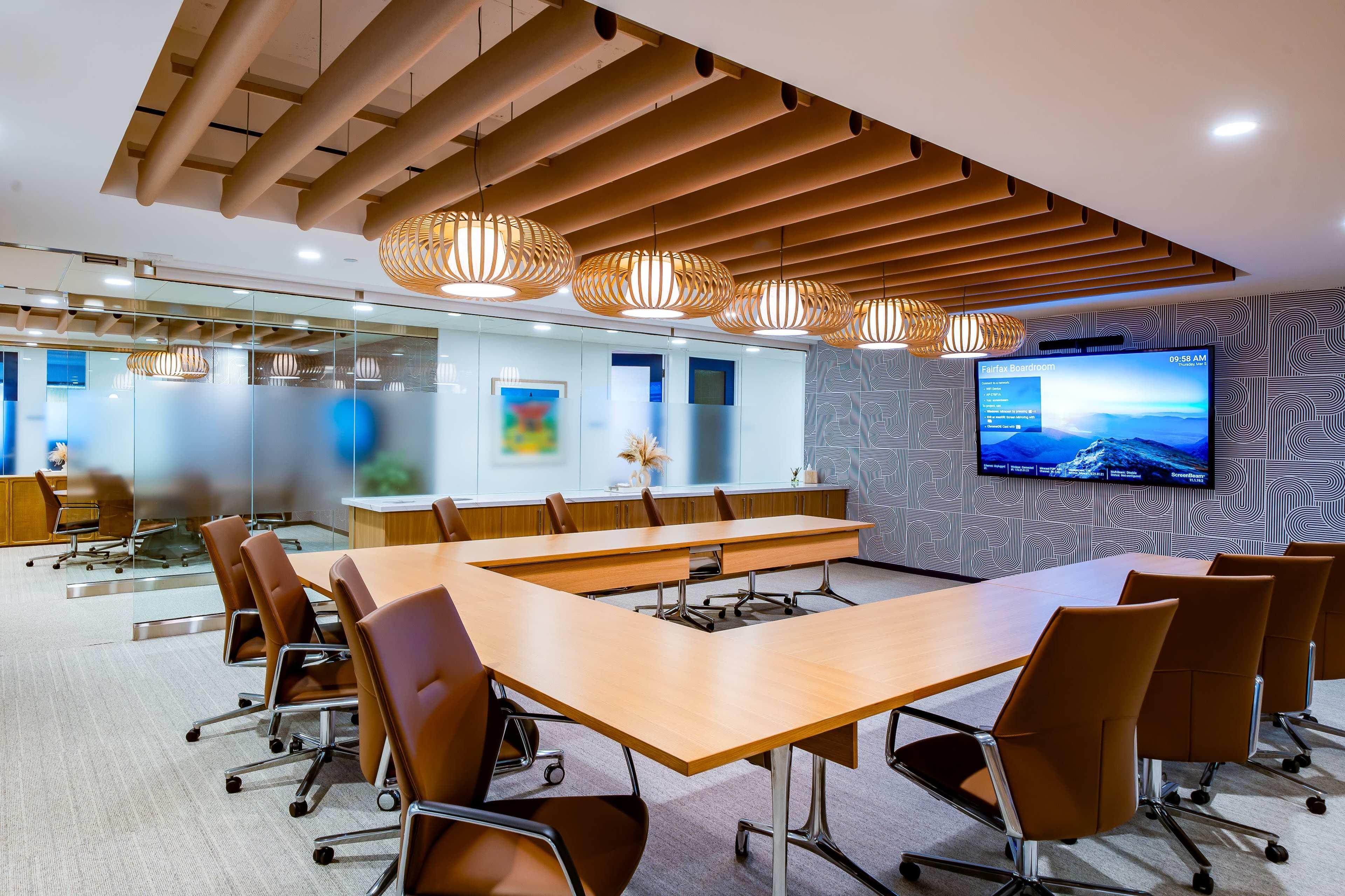The image shows a modern conference room with a large wooden table, leather chairs, and an electronic screen on the wall, illuminated by decorative pendant lights.