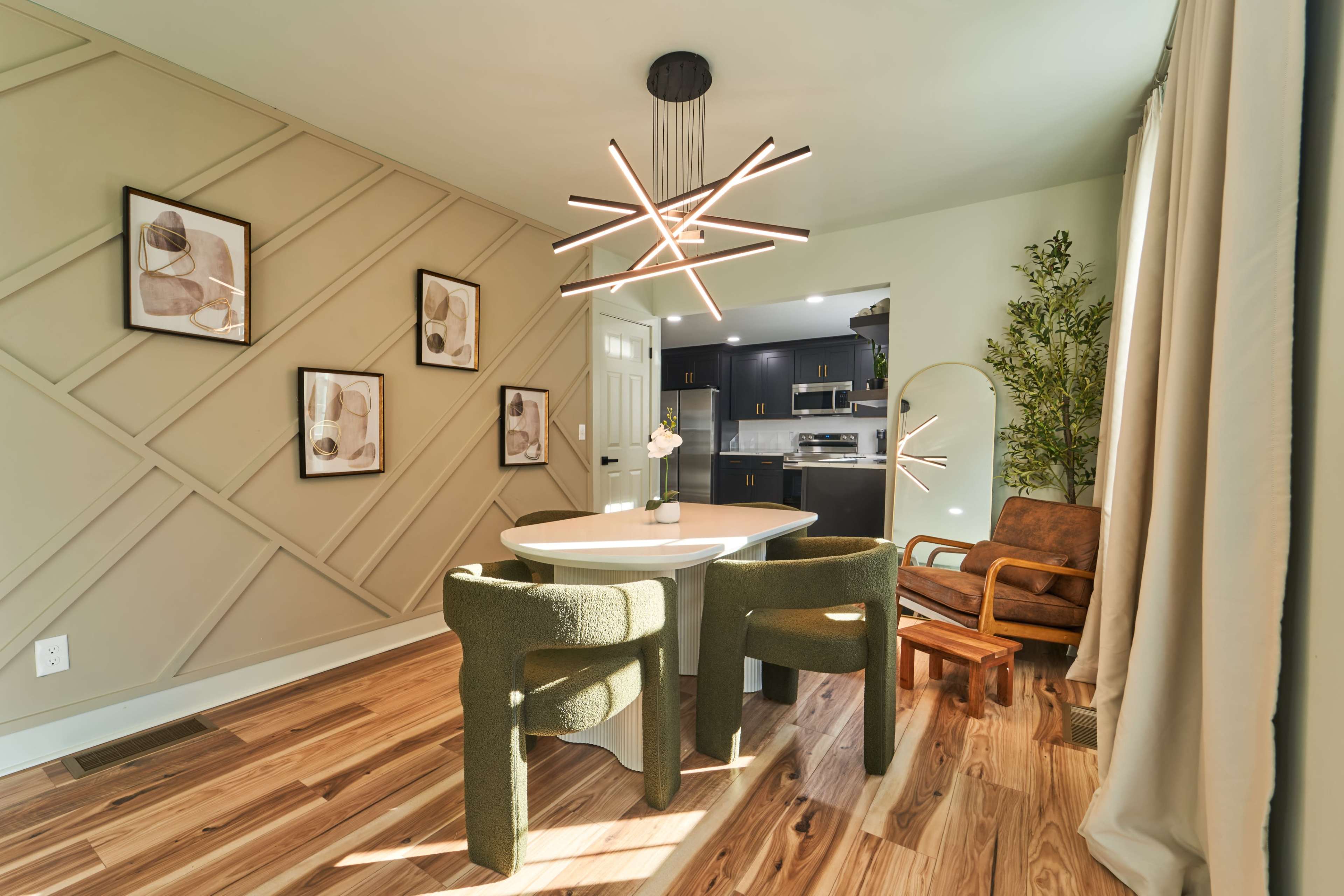 A modern dining area features a round table surrounded by green chairs, with geometric wall art and a unique light fixture.