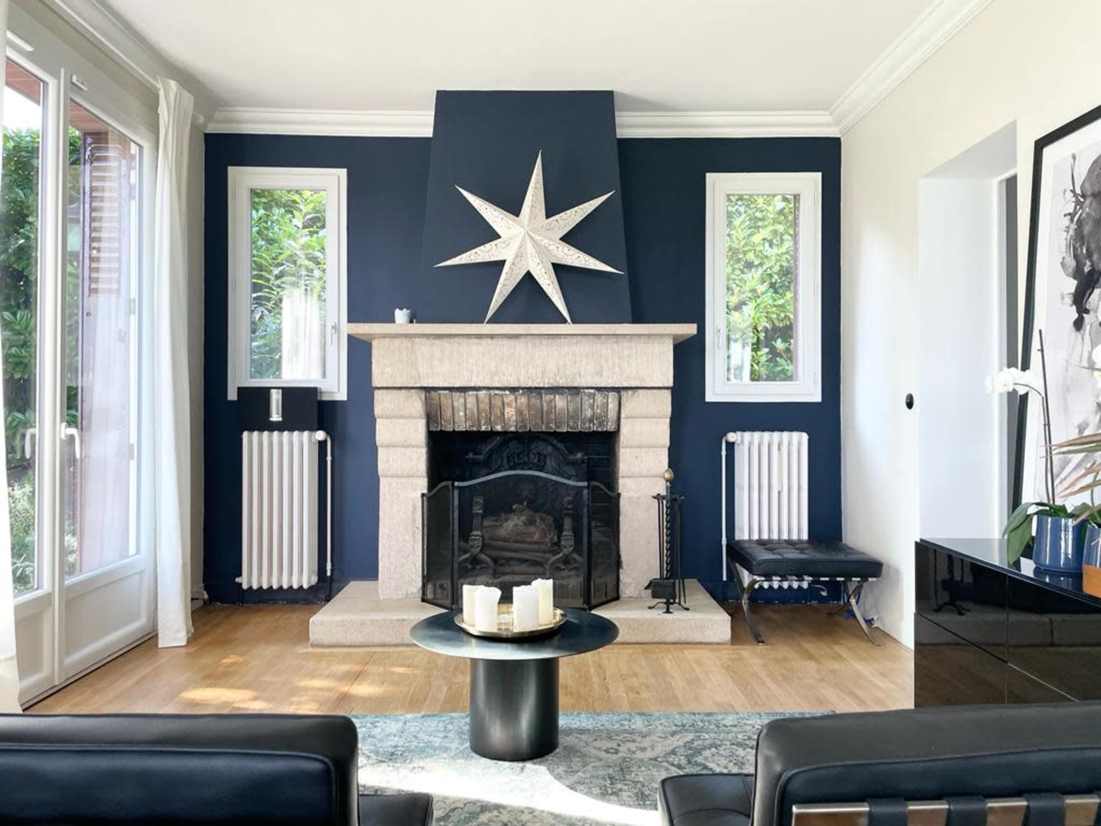 A modern living room featuring a stone fireplace with a star decoration on the wall, large windows, and a coffee table in front of a seating area.