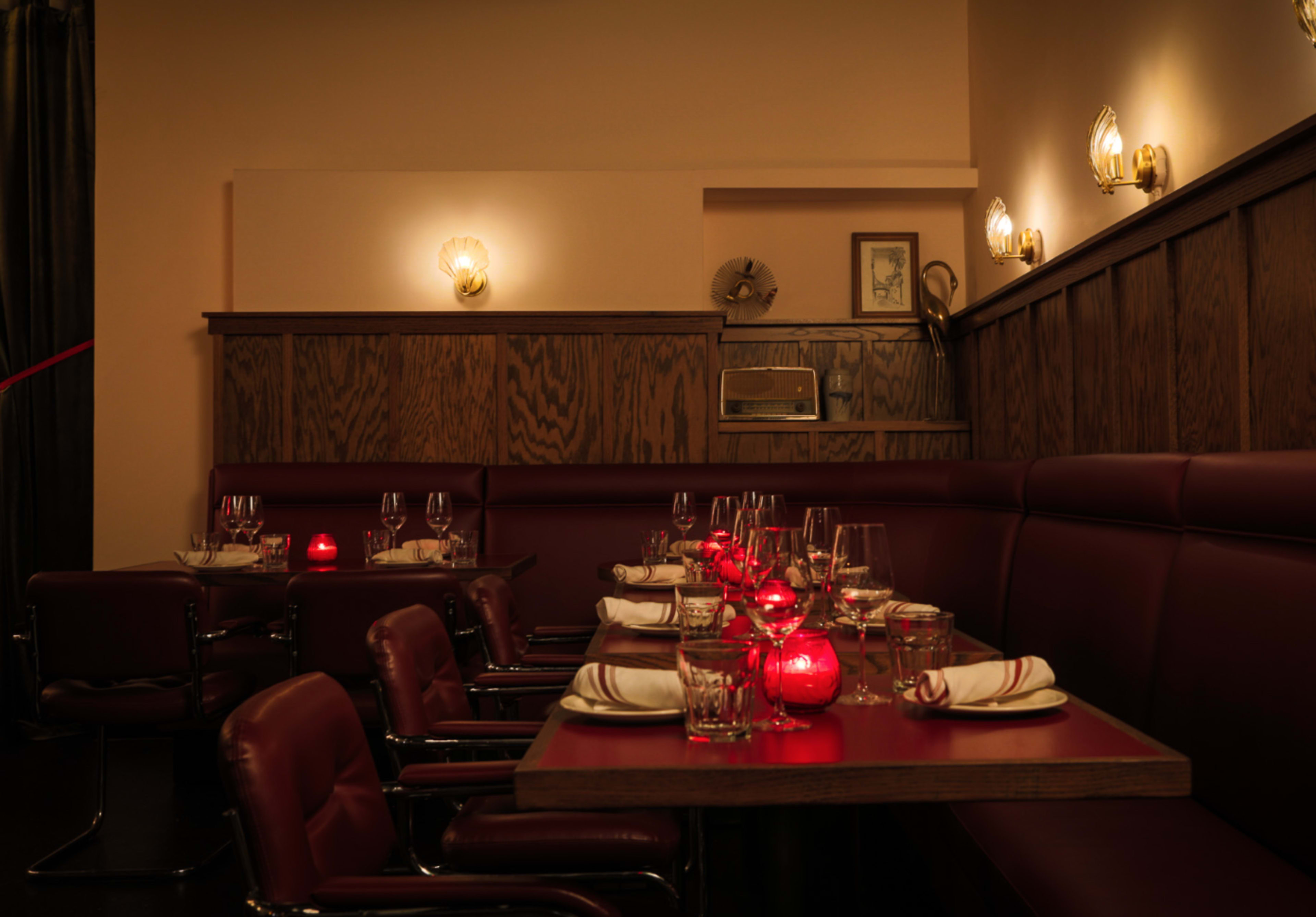 The image shows an intimate restaurant setting with red candles on tables, dark wooden paneling, and cozy seating arrangements.