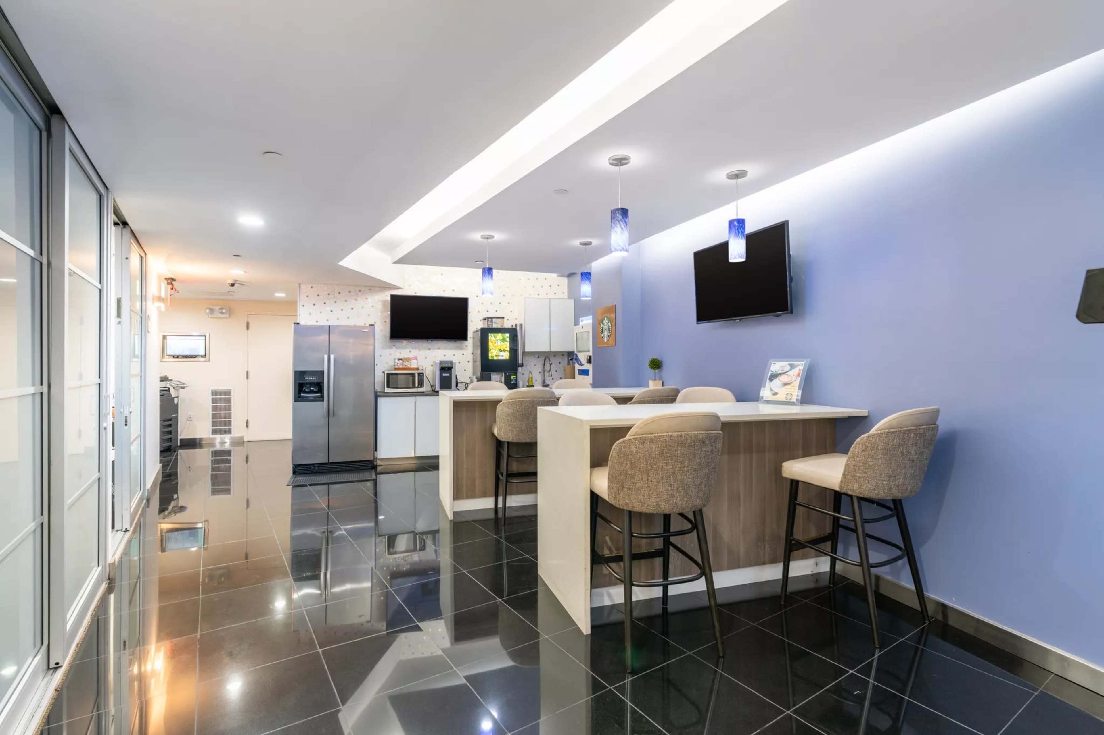 The image shows a modern kitchen area with bar seating, appliances, and a sleek black tile floor.