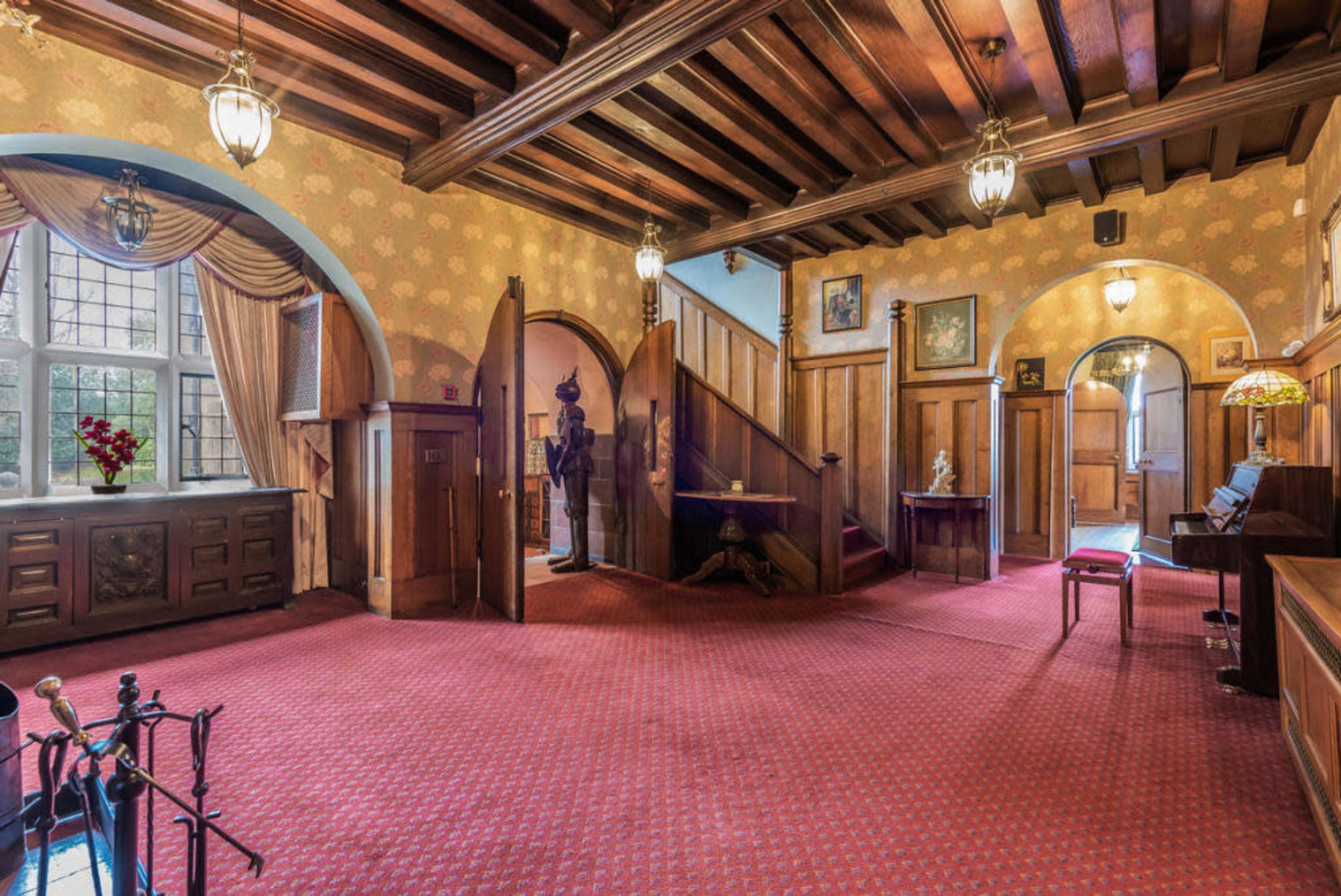 A spacious entryway with wooden beams, wallpaper, and a central staircase leading to an upper level.