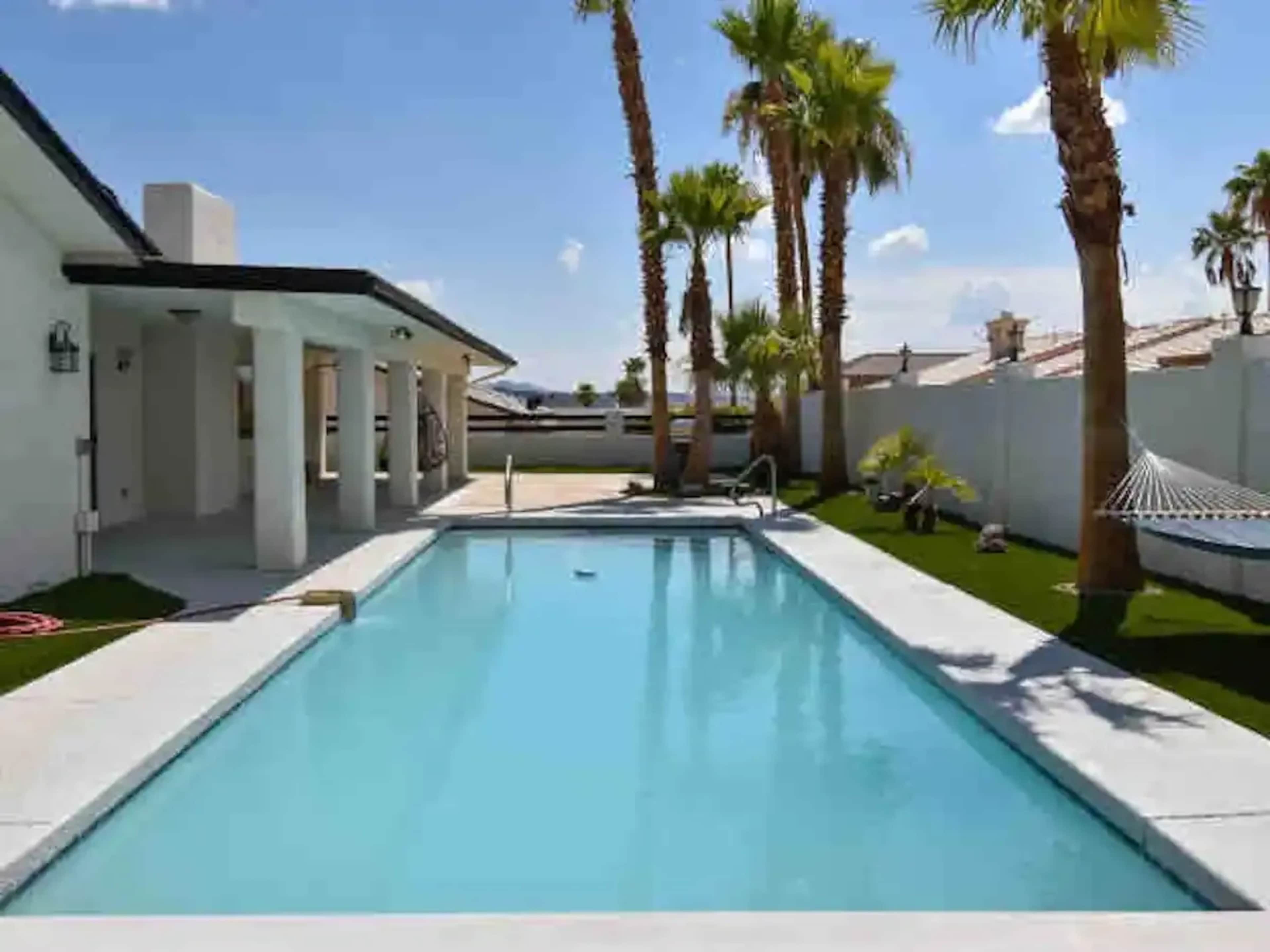 A swimming pool surrounded by palm trees and a white patio area.