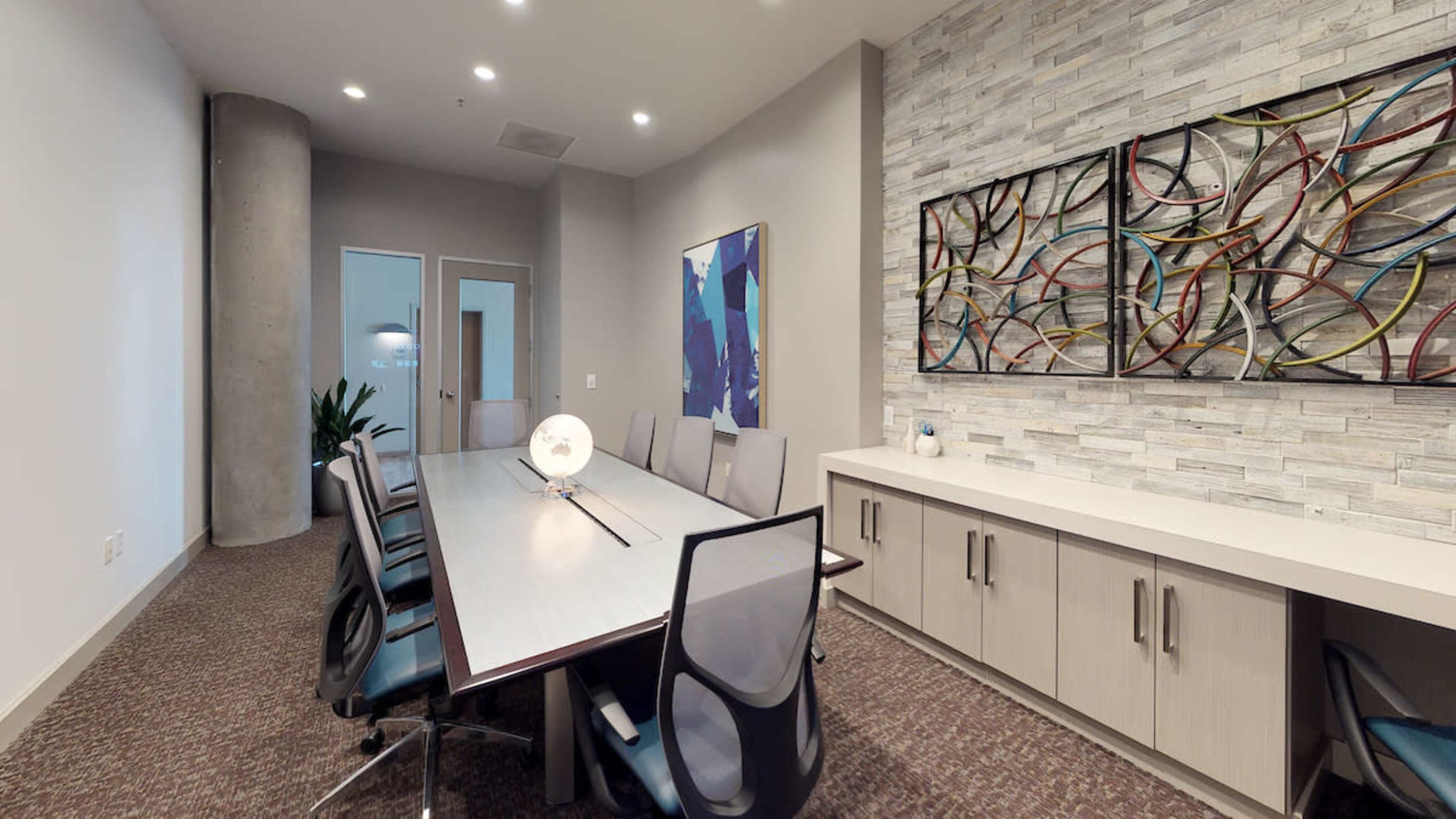 A conference room with a long table, several chairs, modern wall art, and a stone feature wall.