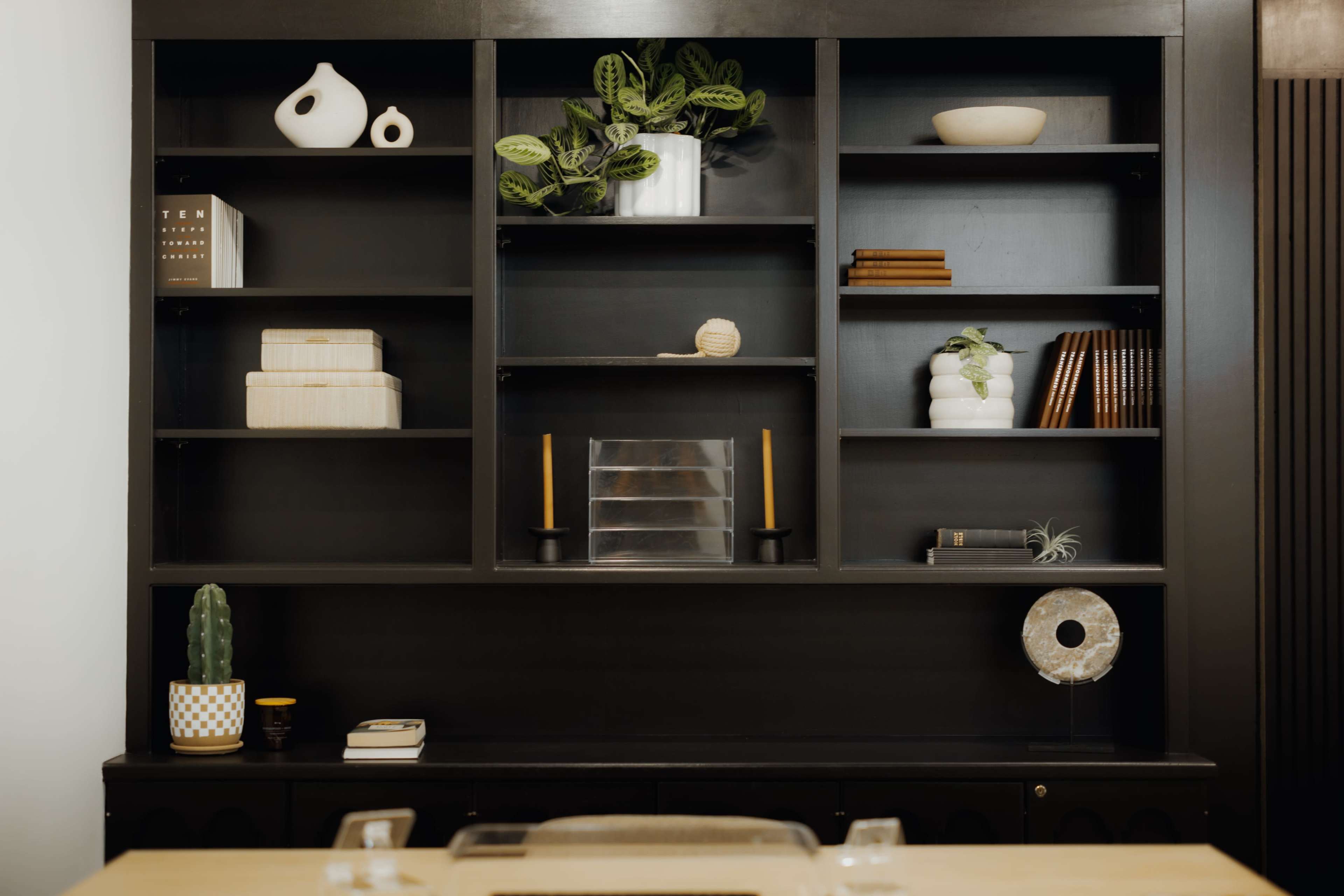 A black bookshelf features various decorative items, plants, and books arranged on its shelves.