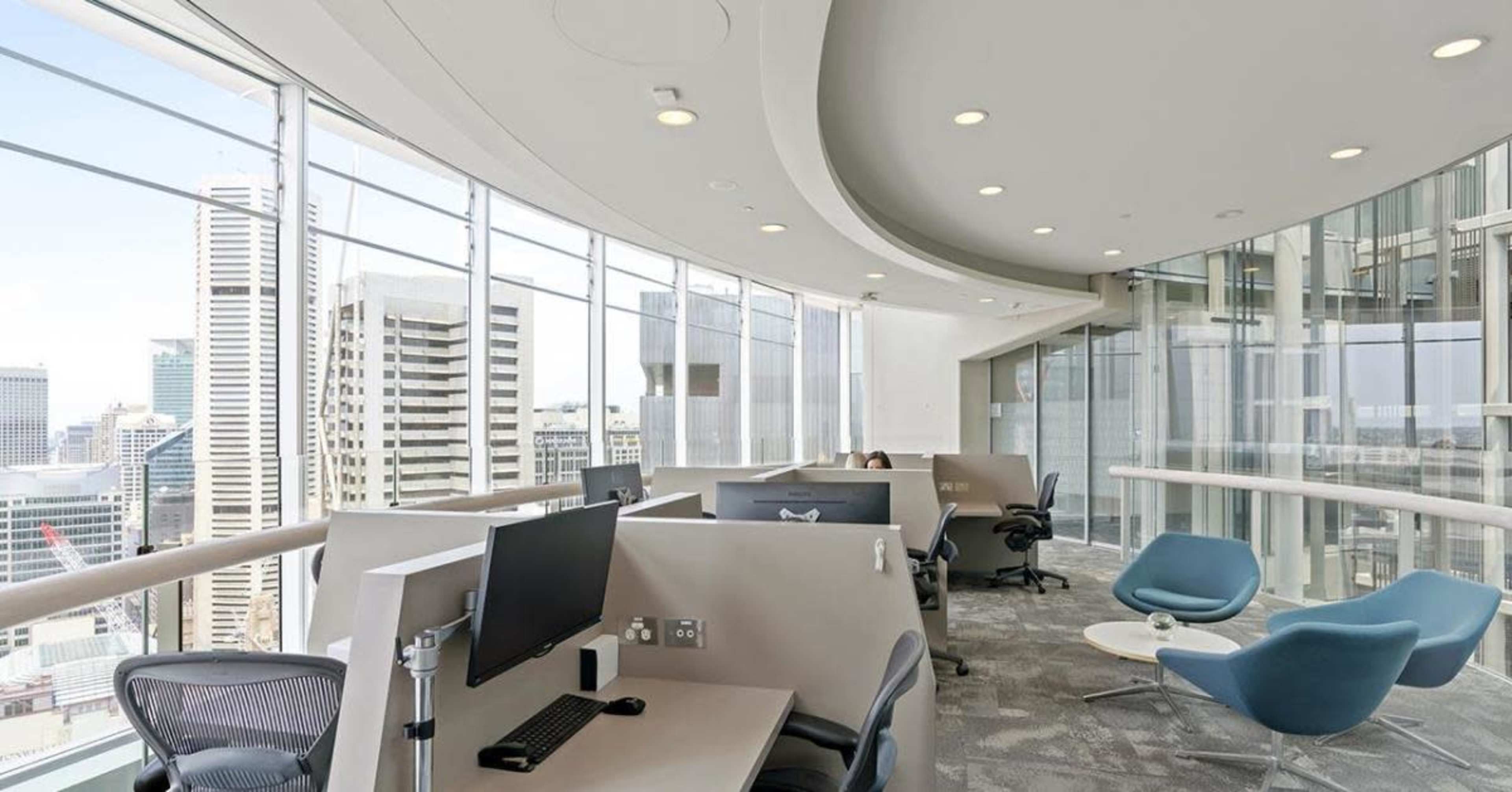 A modern office space with workstations, large windows, and a view of a skyline.