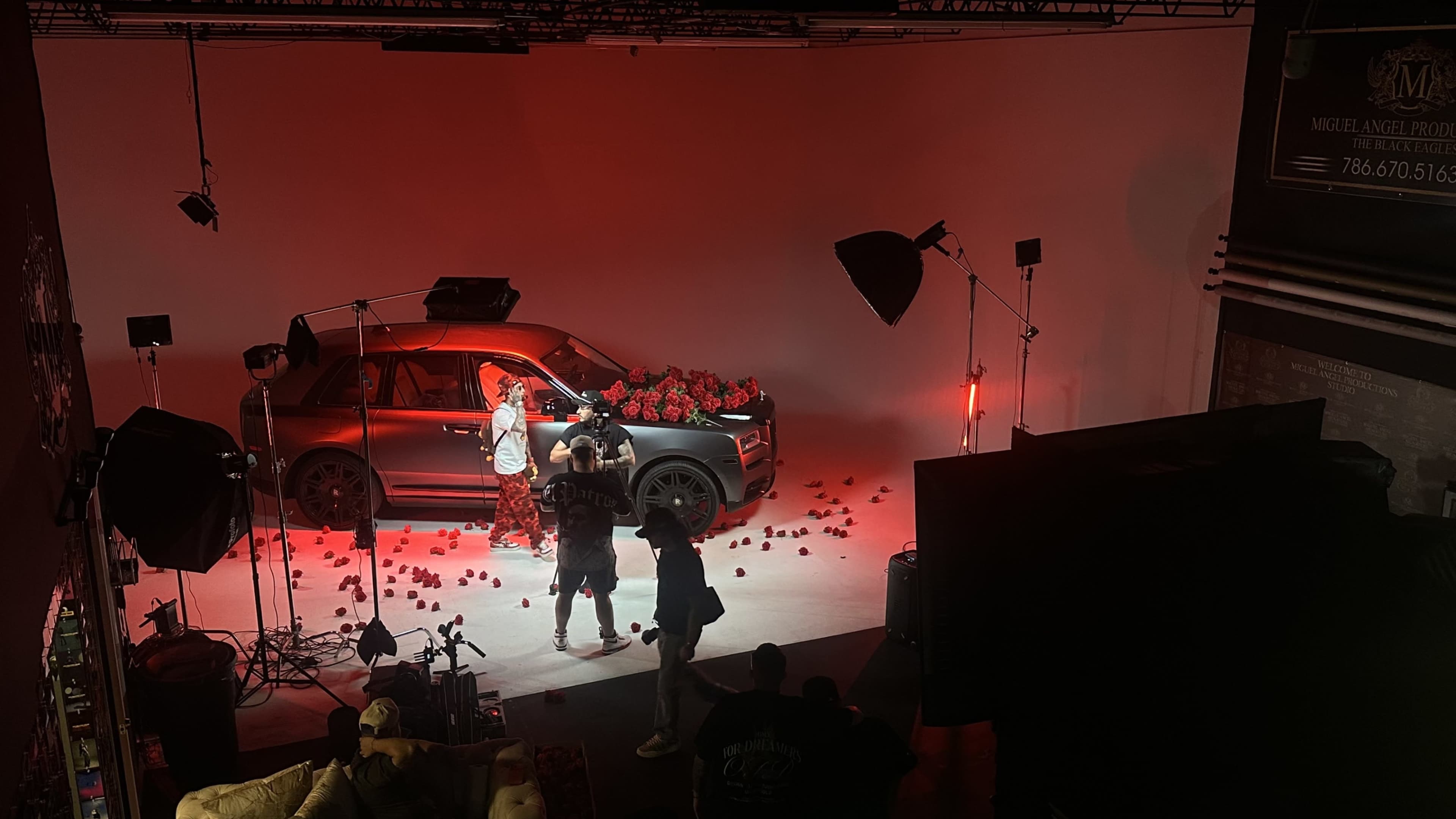A person is posing next to a car adorned with red roses in a studio setting with multiple lighting setups.