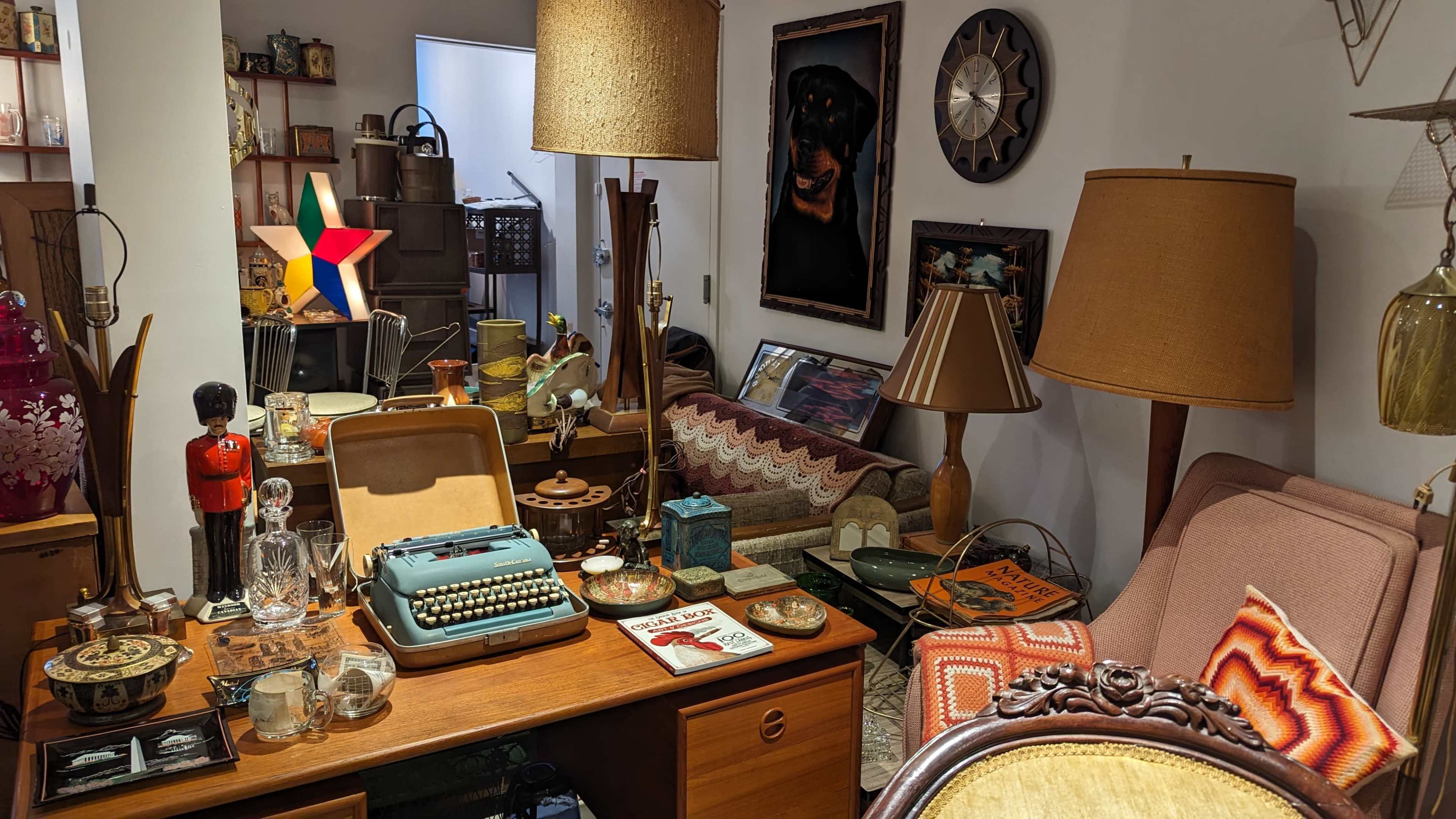 The scene features a cluttered vintage living room with various antique items, including a typewriter, lamps, and decorative artwork.