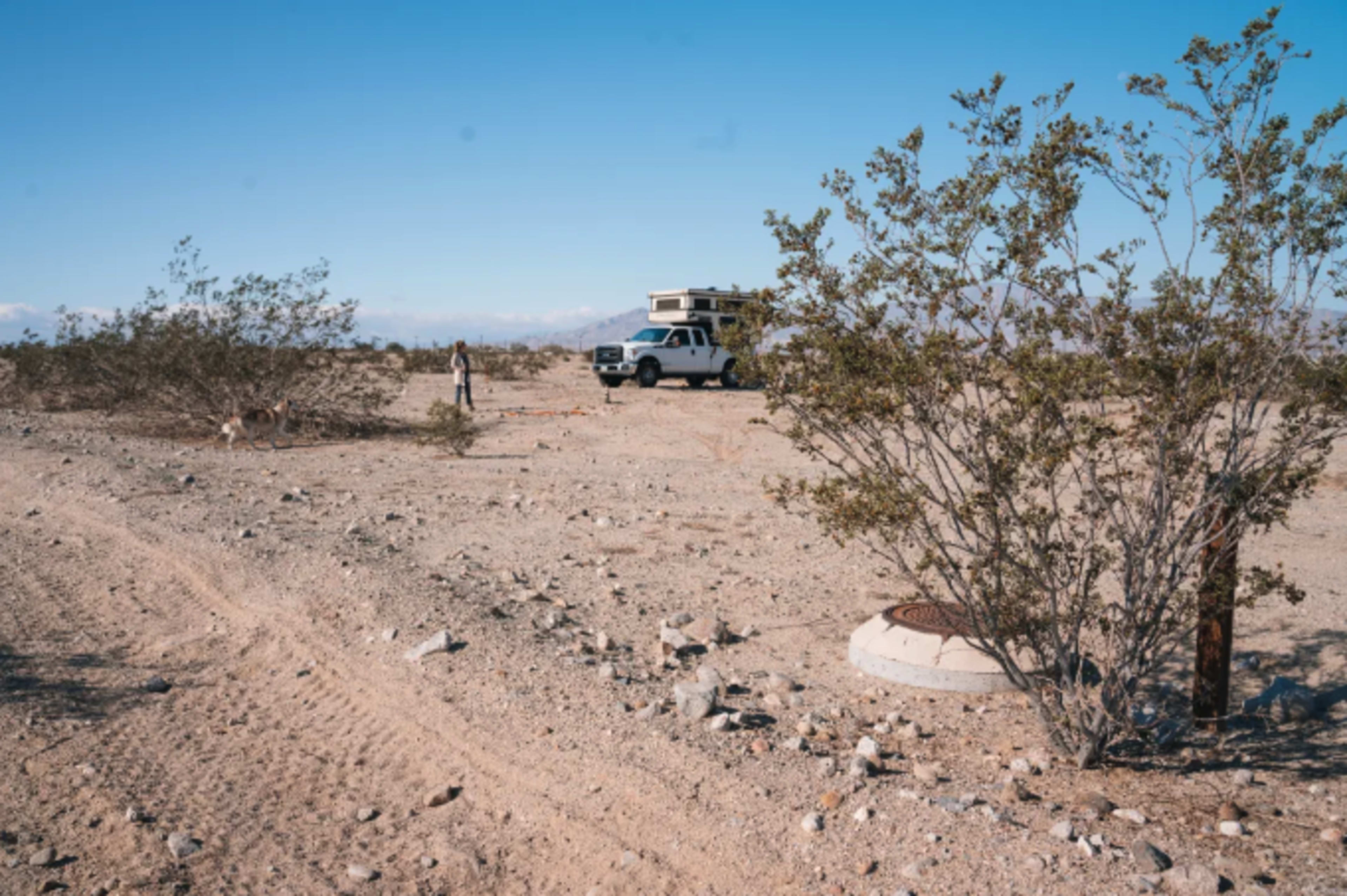 A camper is parked on a gravelly desert landscape, surrounded by sparse vegetation and scattered rocks.