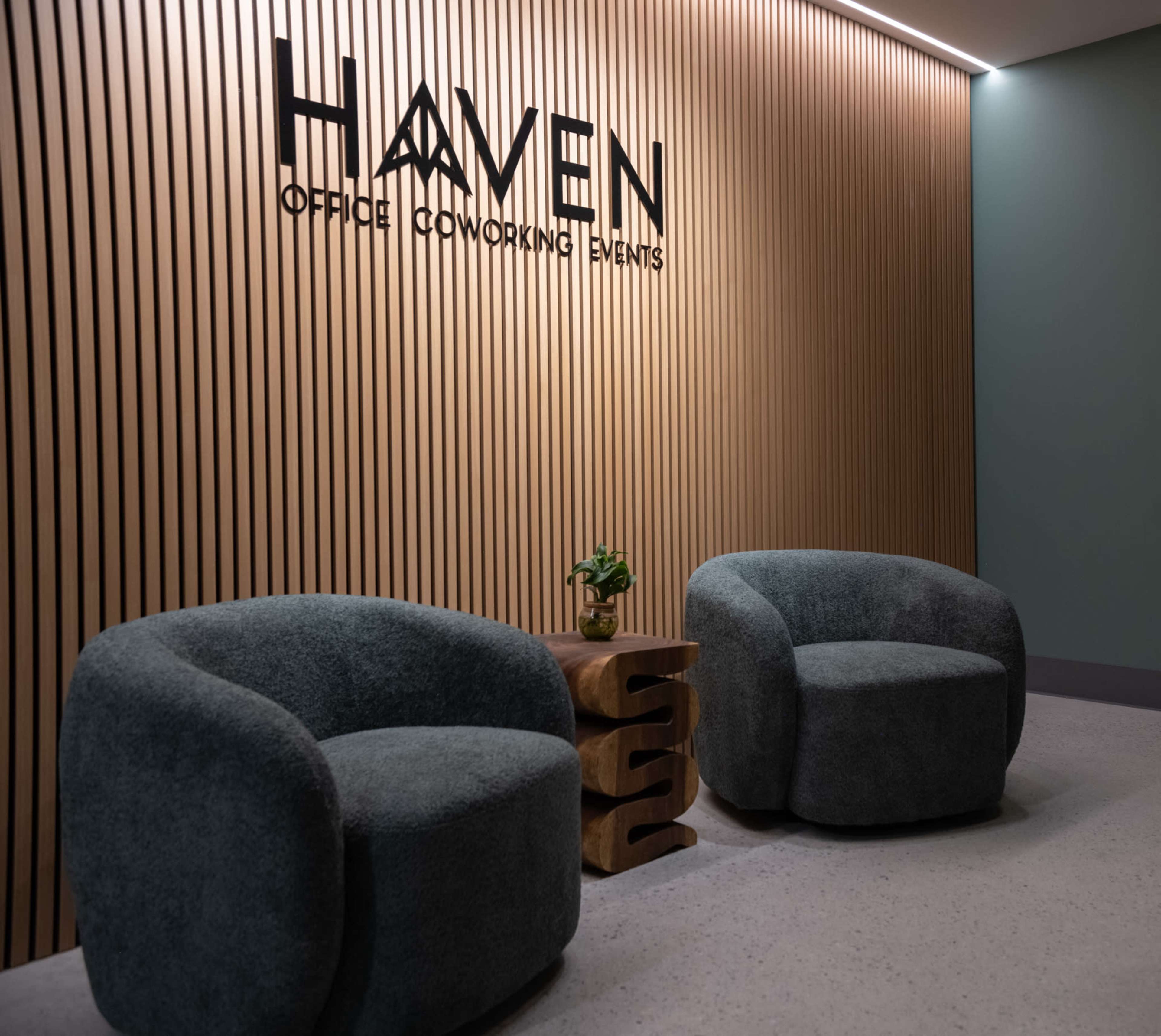 The image features a modern seating area with two round, plush chairs and a small wooden table, set against a backdrop of wooden paneling and a green wall.
