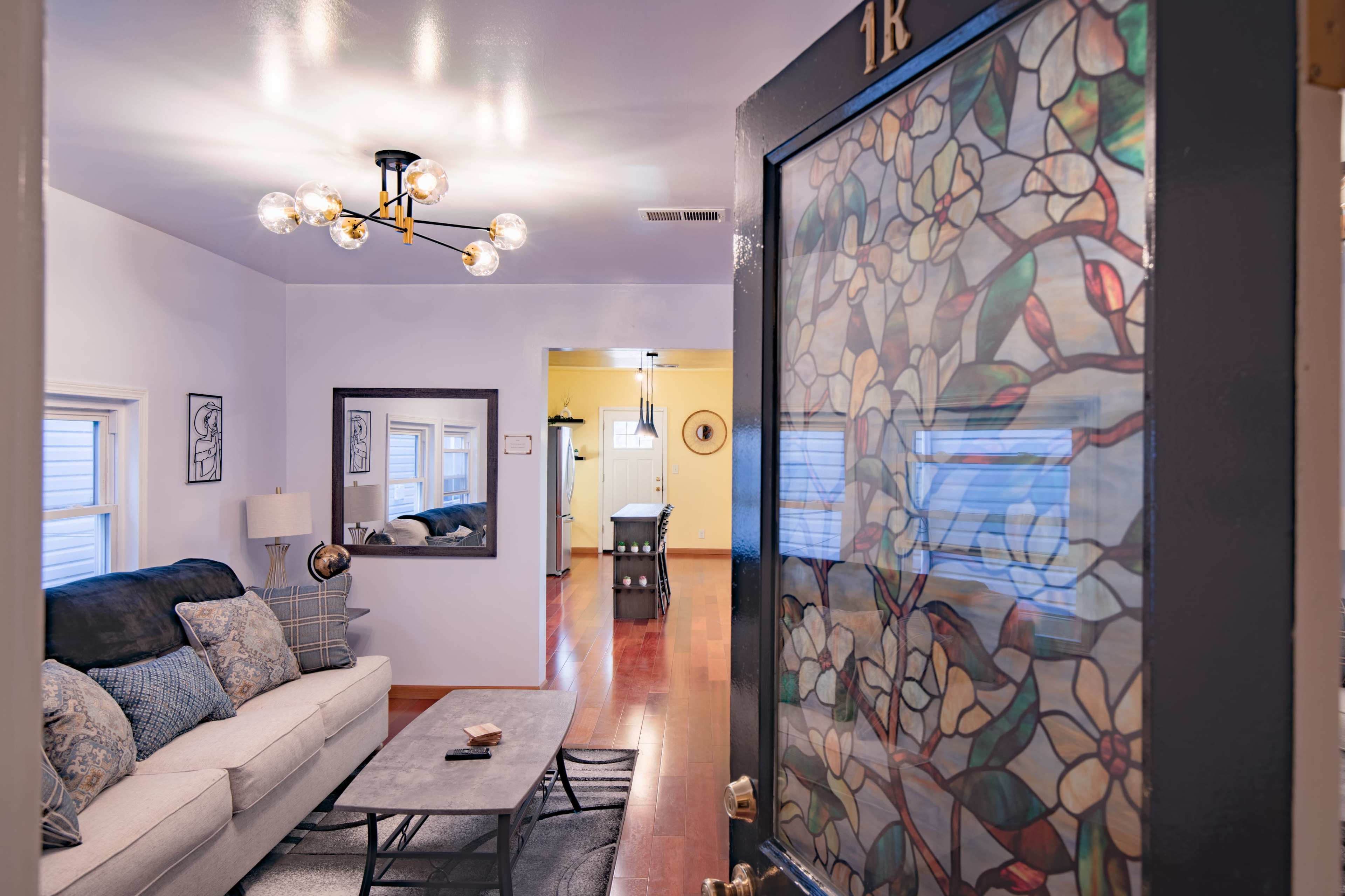 The image shows a living room with a sofa and coffee table, viewed through a door featuring a stained glass window of flowers.