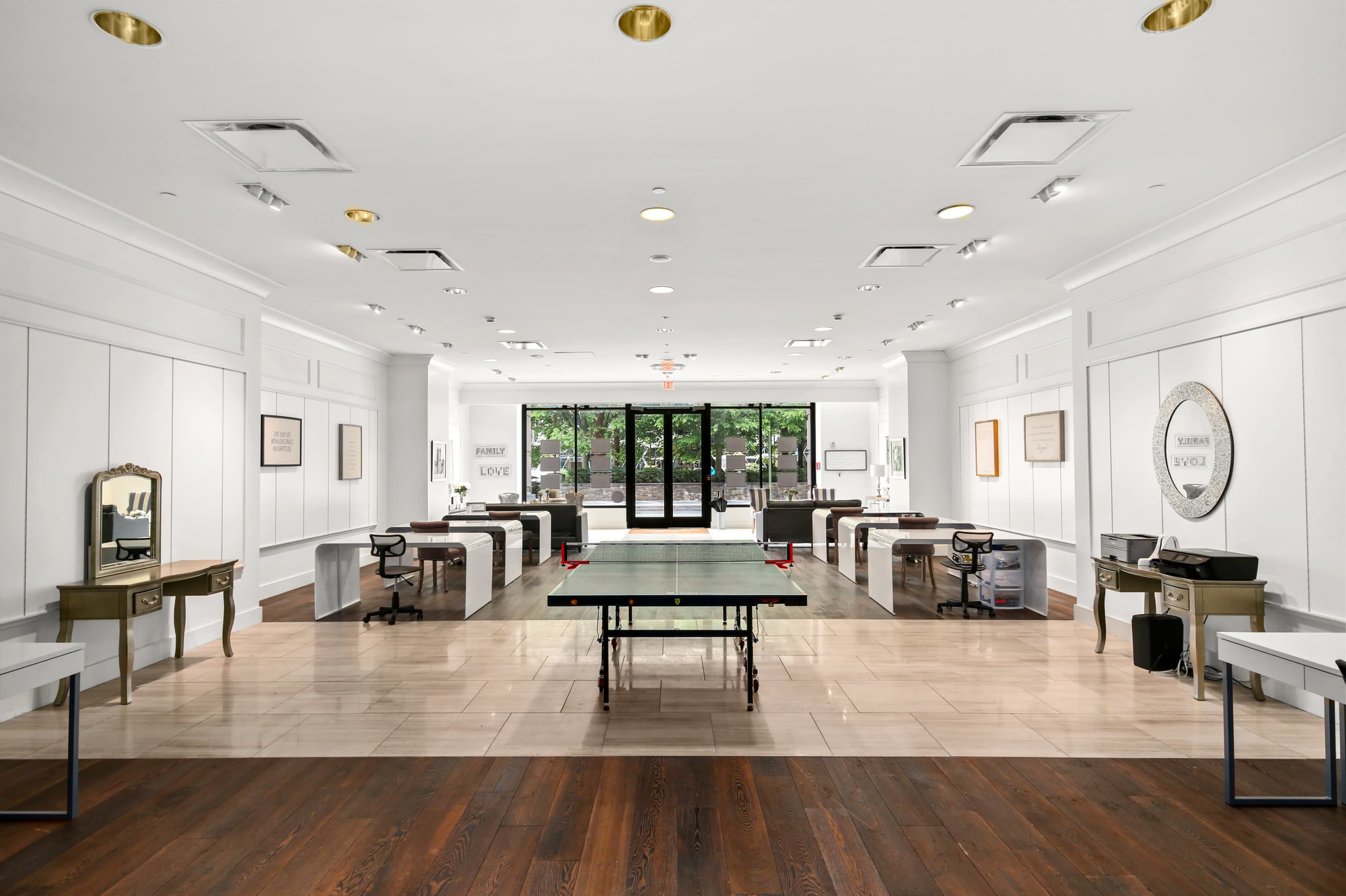 A spacious, modern office with a ping pong table in the center and several desks arranged along the walls.