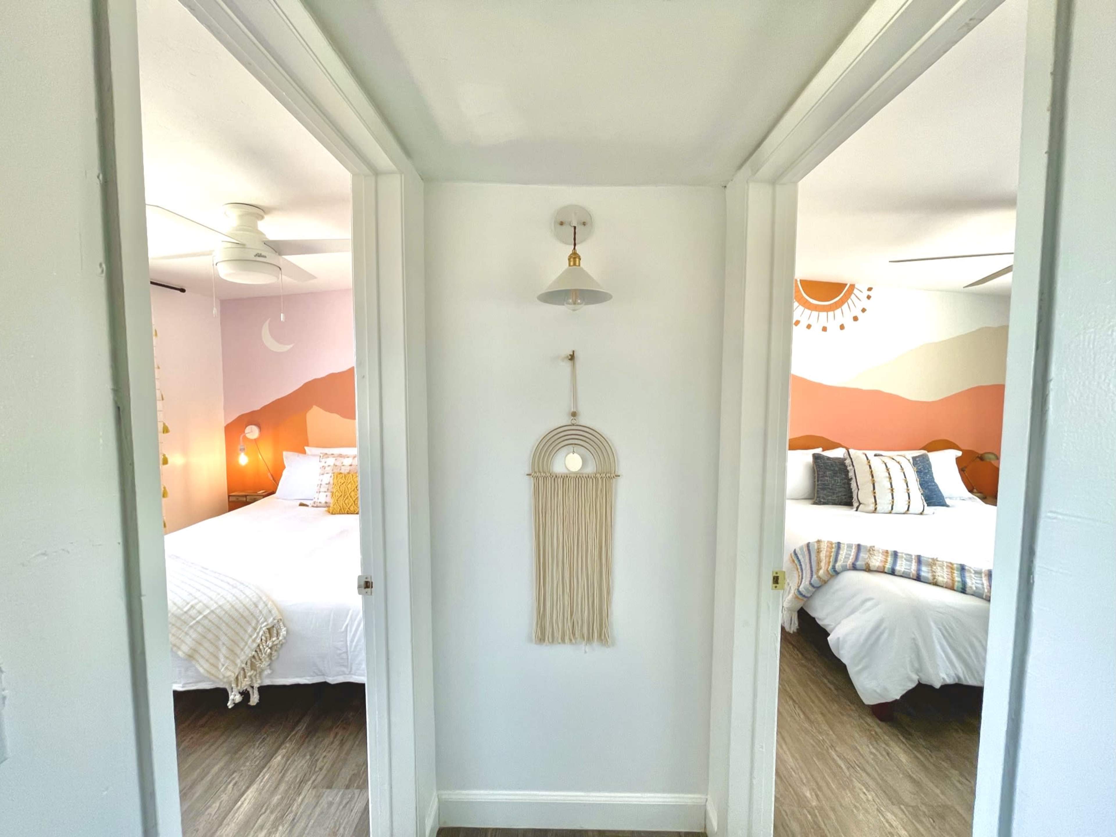 The image shows a hallway with two doors leading to separate bedrooms, featuring a decorative wall hanging in the center.