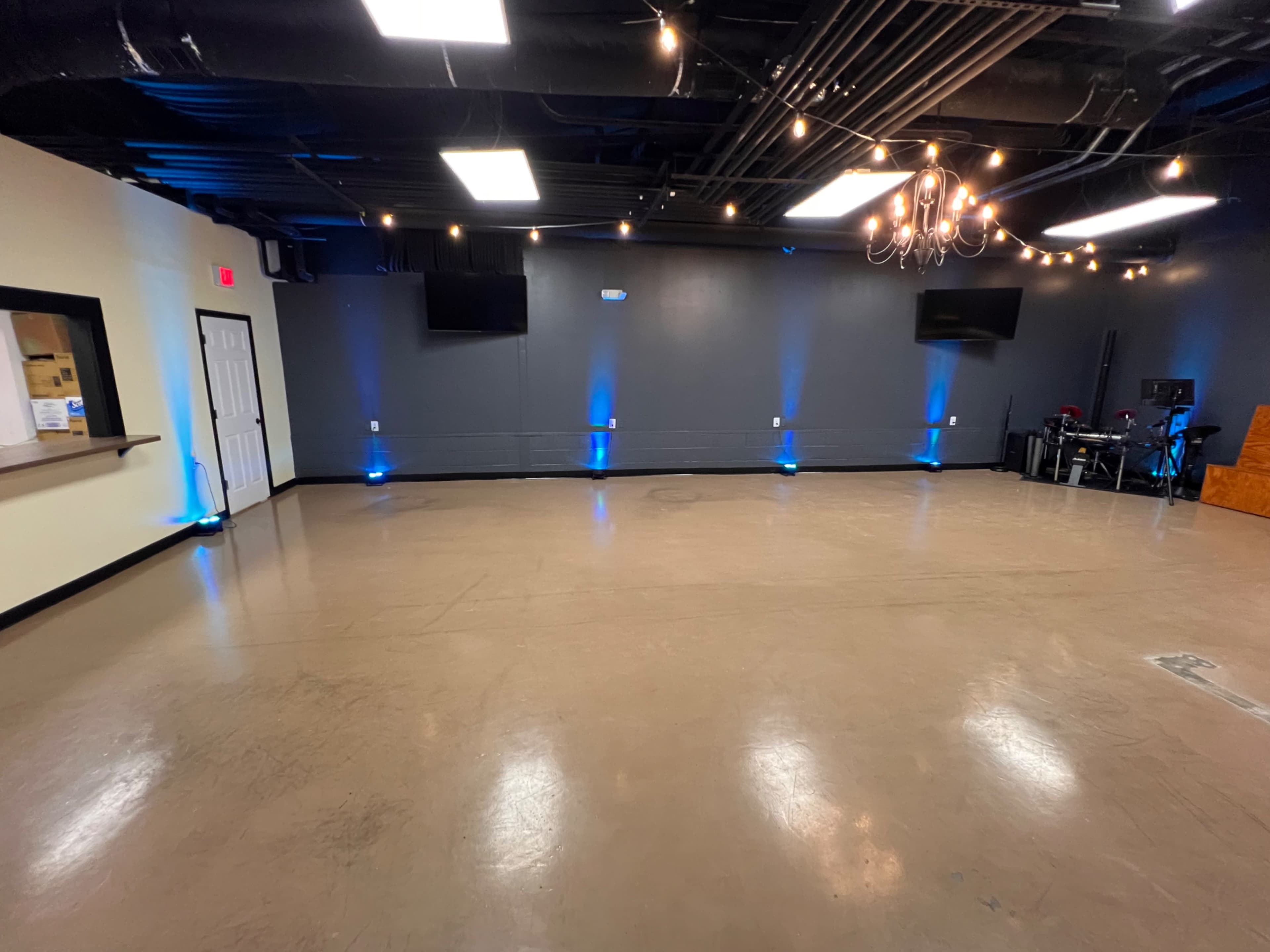 An empty room with a concrete floor, dim blue lighting along the walls, and several hanging light fixtures.