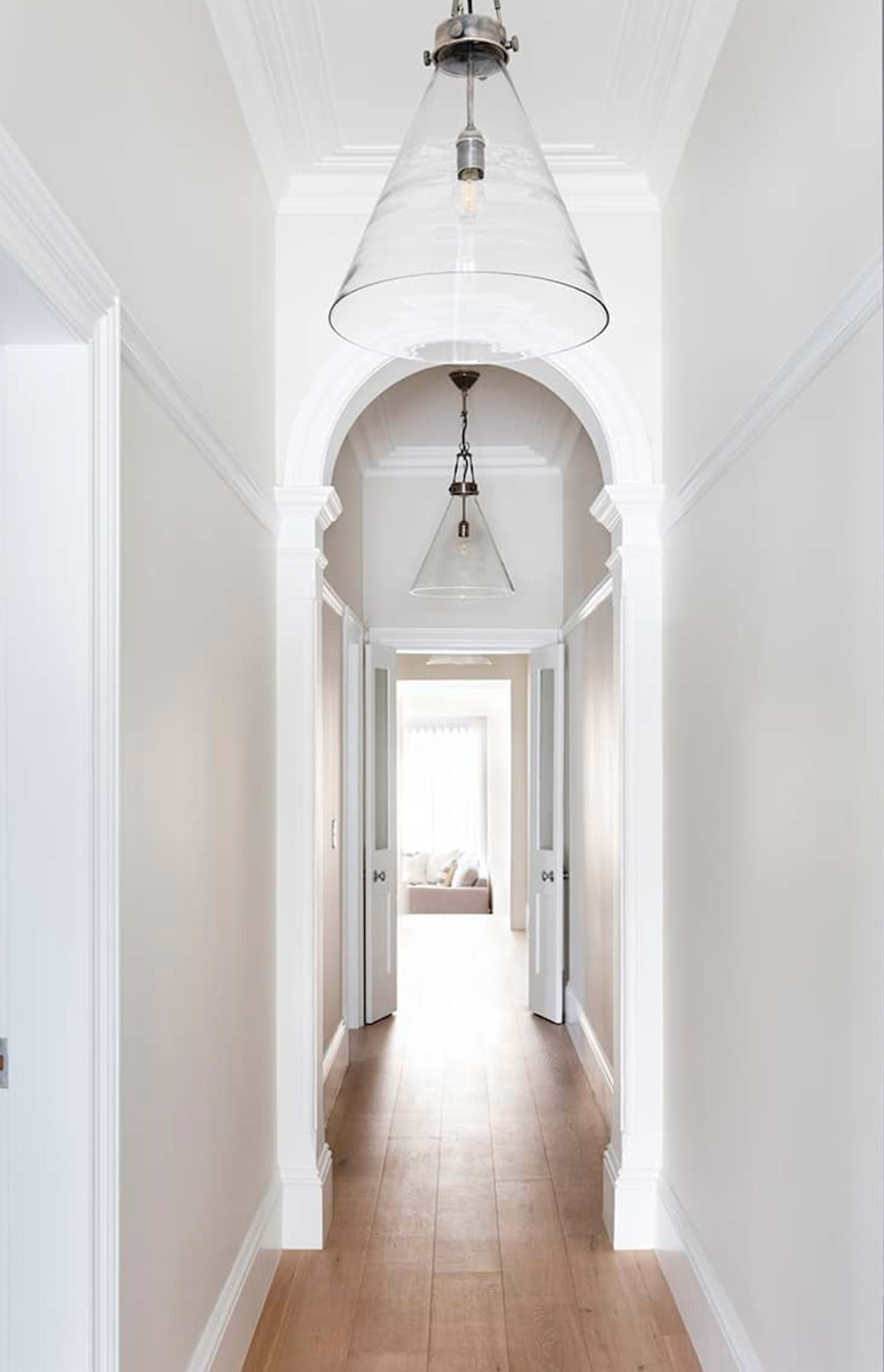 A well-lit hallway features arched doorways and pendant lights, leading towards a bright room at the end.